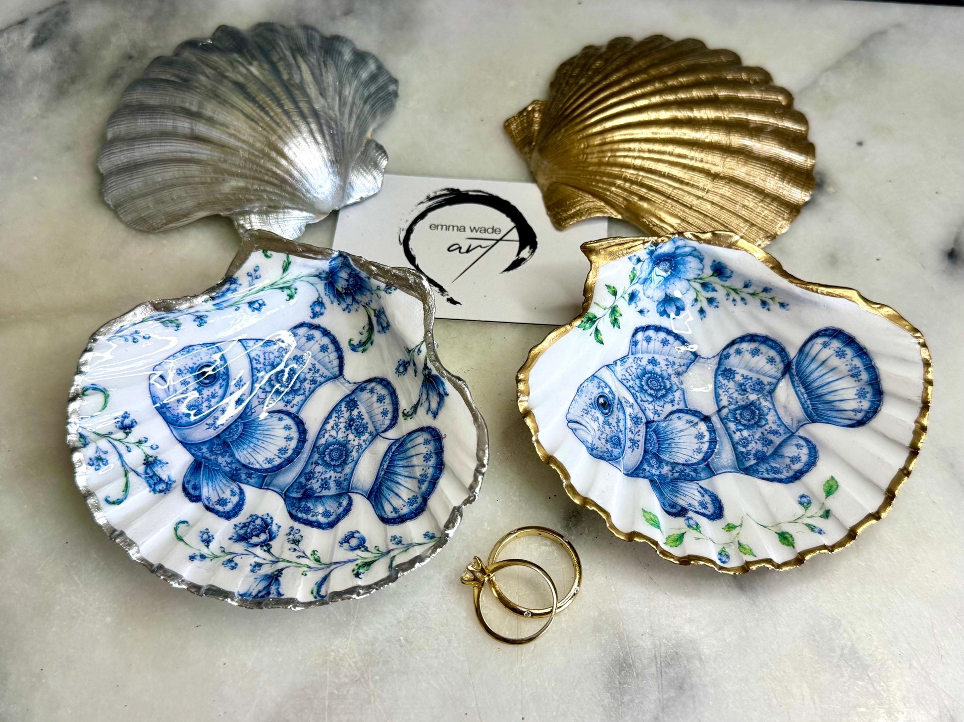 Clownfish scallop shell trinket dish featuring an original illustrated Delft Blue design by Emma Wade ART. Natural scallop shell finished with gold leaf or silver leaf edging and a crystal-clear glossy resin coating. Coastal jewellery tray, Floral ring holder and ocean-inspired gift for fish and sea lovers, beach house décor, weddings, bridesmaids and nautical homes.