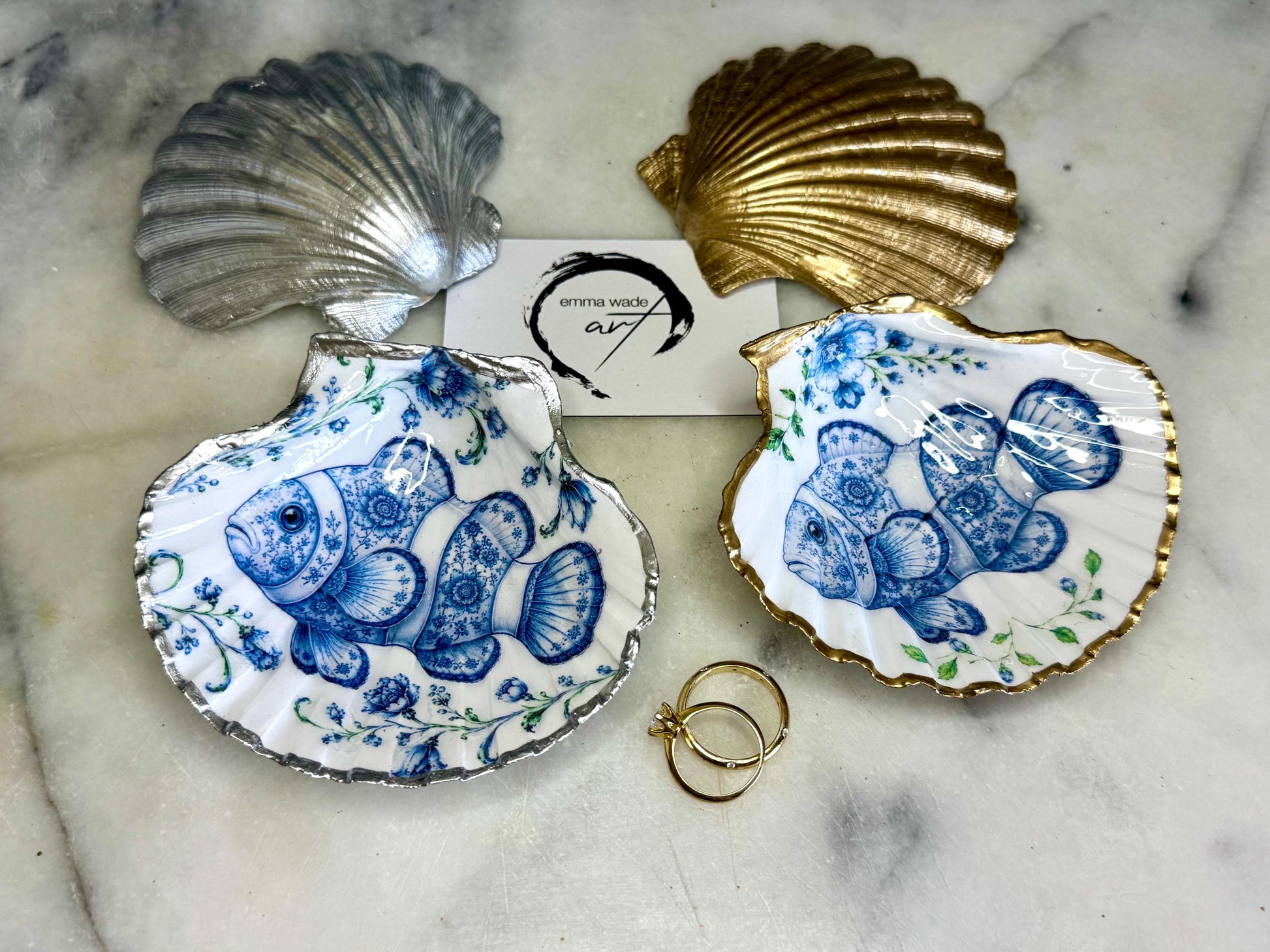 Clownfish scallop shell trinket dish featuring an original illustrated Delft Blue design by Emma Wade ART. Natural scallop shell finished with gold leaf or silver leaf edging and a crystal-clear glossy resin coating. Coastal jewellery tray, Floral ring holder and ocean-inspired gift for fish and sea lovers, beach house décor, weddings, bridesmaids and nautical homes.