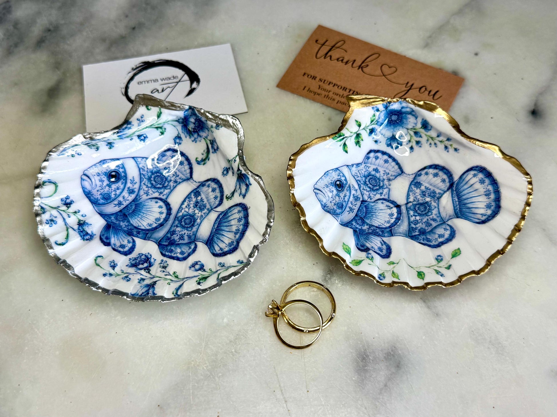 Clownfish scallop shell trinket dish featuring an original illustrated Delft Blue design by Emma Wade ART. Natural scallop shell finished with gold leaf or silver leaf edging and a crystal-clear glossy resin coating. Coastal jewellery tray, Floral ring holder and ocean-inspired gift for fish and sea lovers, beach house décor, weddings, bridesmaids and nautical homes.