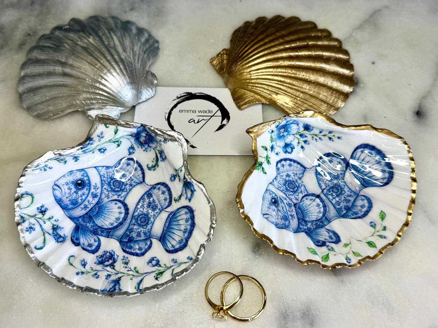 Clownfish scallop shell trinket dish featuring an original illustrated Delft Blue design by Emma Wade ART. Natural scallop shell finished with gold leaf or silver leaf edging and a crystal-clear glossy resin coating. Coastal jewellery tray, Floral ring holder and ocean-inspired gift for fish and sea lovers, beach house décor, weddings, bridesmaids and nautical homes.