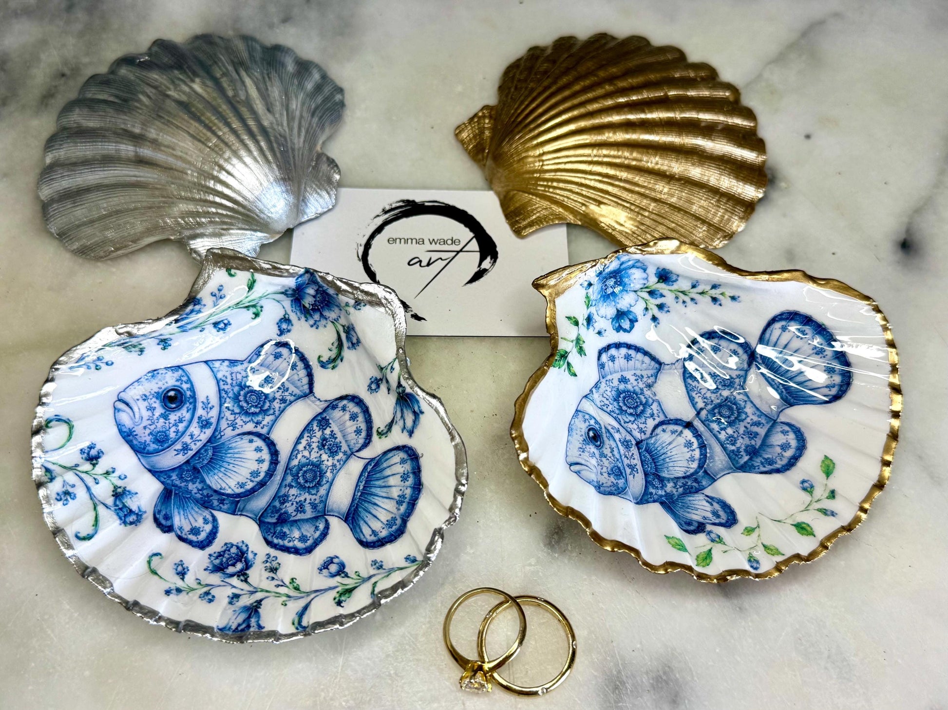 Clownfish scallop shell trinket dish featuring an original illustrated Delft Blue design by Emma Wade ART. Natural scallop shell finished with gold leaf or silver leaf edging and a crystal-clear glossy resin coating. Coastal jewellery tray, Floral ring holder and ocean-inspired gift for fish and sea lovers, beach house décor, weddings, bridesmaids and nautical homes.