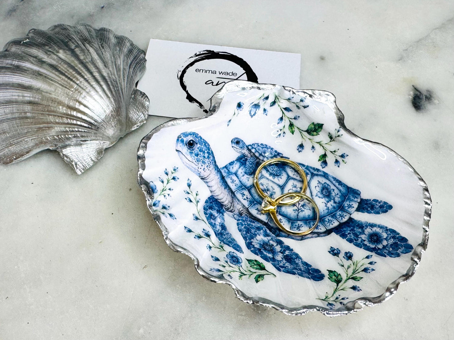 Sea Turtle Mum and Baby scallop shell trinket dish featuring an original illustrated Delft Blue design by Emma Wade ART. Natural scallop shell finished with gold leaf or silver leaf edging and a crystal-clear glossy resin coating. Coastal jewellery tray, ring holder and ocean-inspired gift for sea turtle lovers, beach house décor, weddings, bridesmaids and nautical homes.