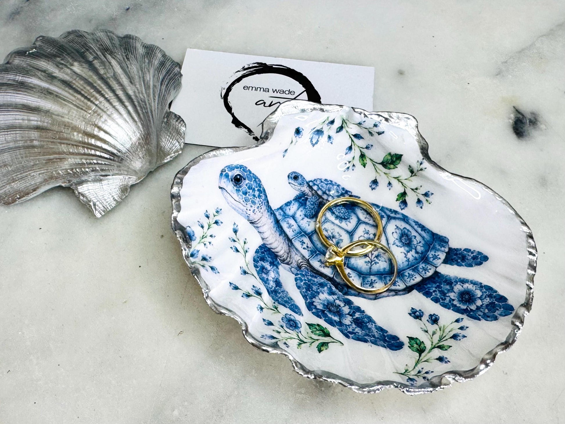 Sea Turtle Mum and Baby scallop shell trinket dish featuring an original illustrated Delft Blue design by Emma Wade ART. Natural scallop shell finished with gold leaf or silver leaf edging and a crystal-clear glossy resin coating. Coastal jewellery tray, ring holder and ocean-inspired gift for sea turtle lovers, beach house décor, weddings, bridesmaids and nautical homes.