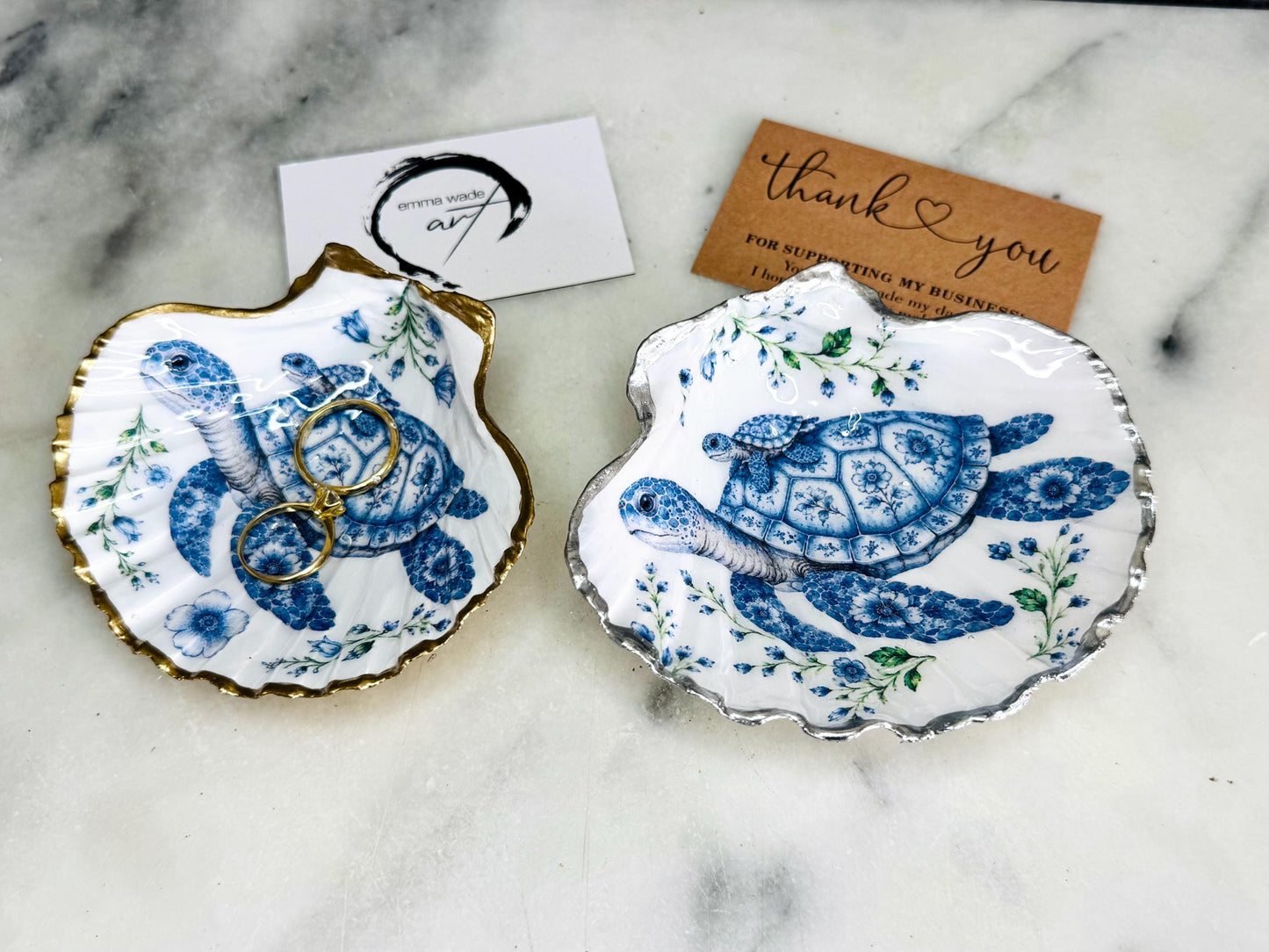 Sea Turtle Mum and Baby scallop shell trinket dish featuring an original illustrated Delft Blue design by Emma Wade ART. Natural scallop shell finished with gold leaf or silver leaf edging and a crystal-clear glossy resin coating. Coastal jewellery tray, ring holder and ocean-inspired gift for sea turtle lovers, beach house décor, weddings, bridesmaids and nautical homes.
