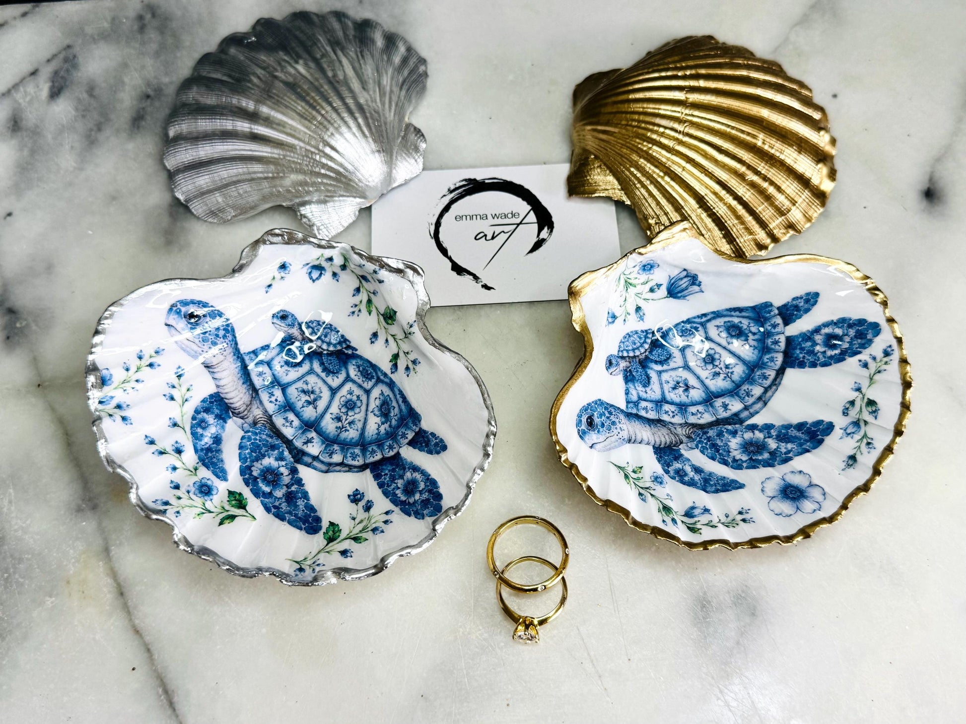 Handcrafted scallop shell trinket dish featuring an original illustrated Delft Blue Sea Turtle design by Emma Wade ART. Natural shell with hand-gilded gold or silver leaf rim and glossy resin finish. Coastal jewellery tray for rings, earrings and keepsakes. Beach house decor, sea life gift and ocean-inspired home accessory available in standard and large sizes.