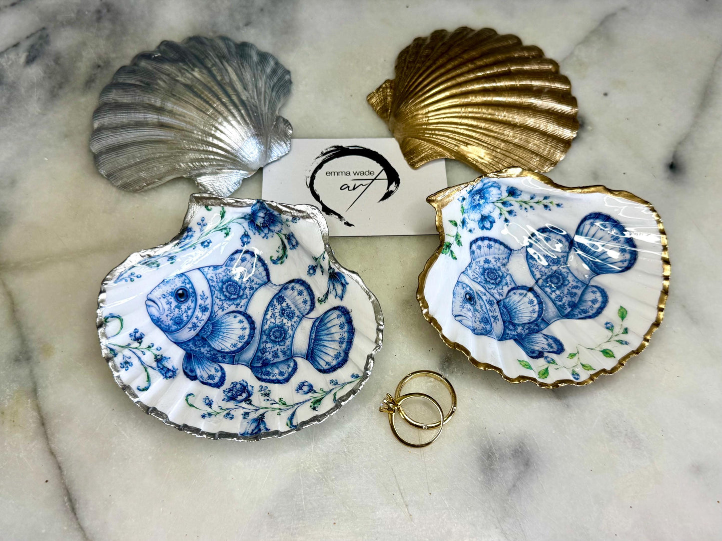 Clownfish scallop shell trinket dish featuring an original illustrated Delft Blue design by Emma Wade ART. Natural scallop shell finished with gold leaf or silver leaf edging and a crystal-clear glossy resin coating. Coastal jewellery tray, ring holder and ocean-inspired gift for fish and sea lovers, beach house décor, weddings, bridesmaids and nautical homes.