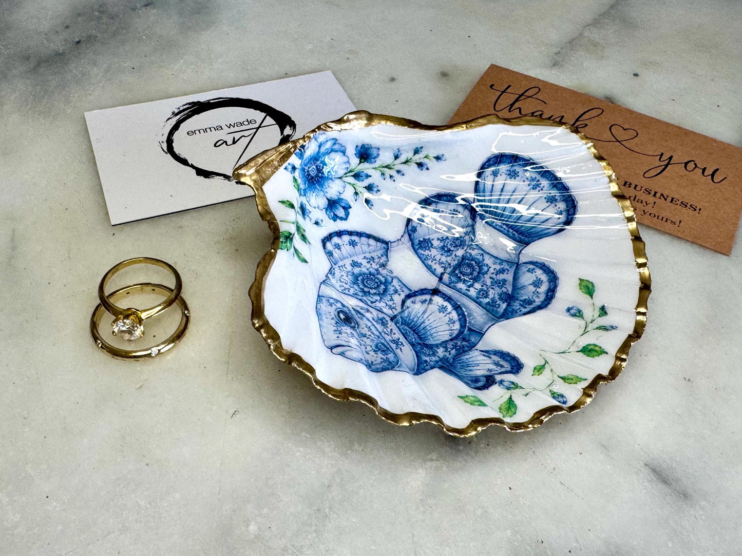 Clownfish scallop shell trinket dish featuring an original illustrated Delft Blue design by Emma Wade ART. Natural scallop shell finished with gold leaf or silver leaf edging and a crystal-clear glossy resin coating. Coastal jewellery tray, Floral ring holder and ocean-inspired gift for fish and sea lovers, beach house décor, weddings, bridesmaids and nautical homes.