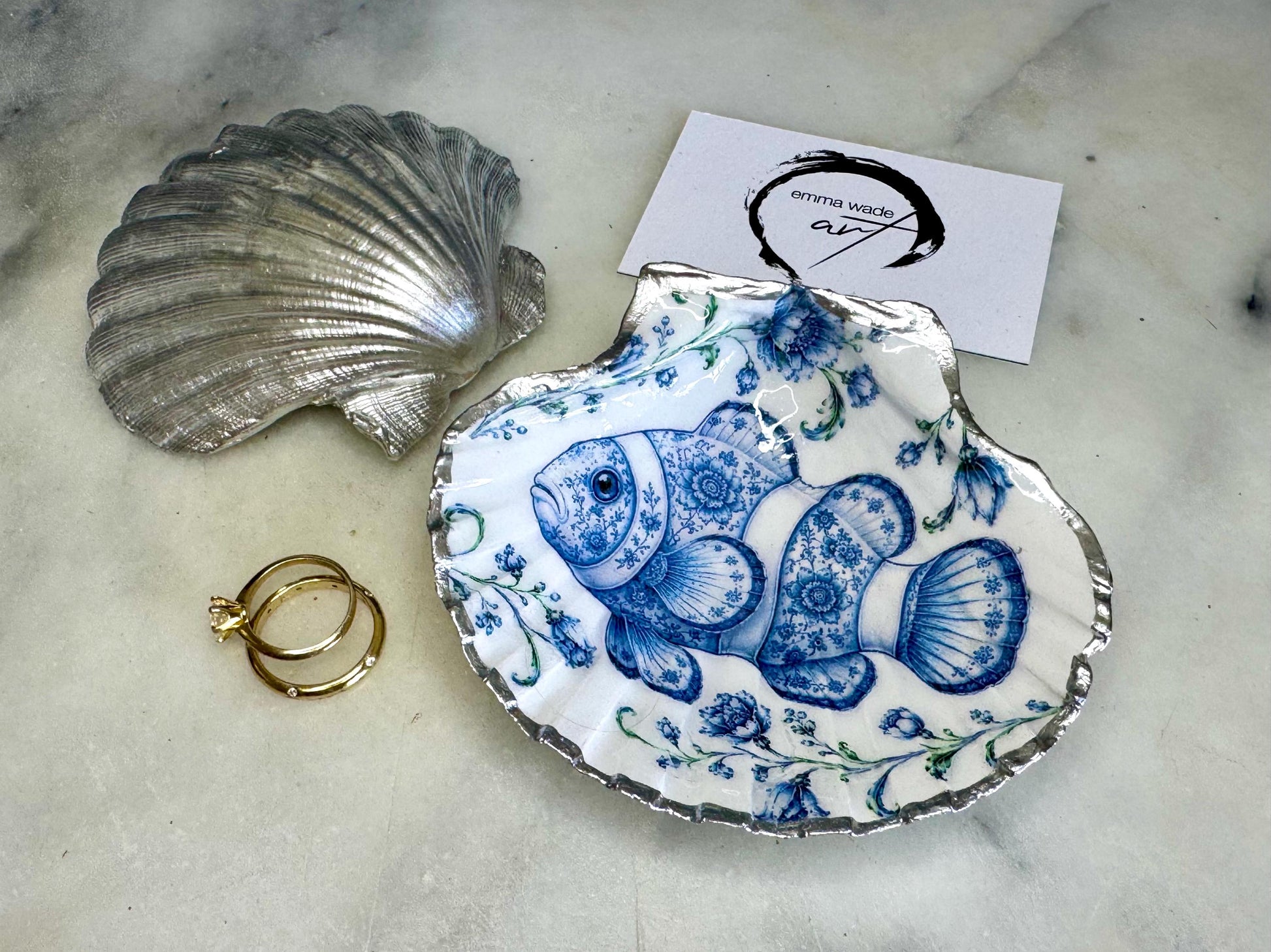 Clownfish scallop shell trinket dish featuring an original illustrated Delft Blue design by Emma Wade ART. Natural scallop shell finished with gold leaf or silver leaf edging and a crystal-clear glossy resin coating. Coastal jewellery tray, ring holder and ocean-inspired gift for fish and sea lovers, beach house décor, weddings, bridesmaids and nautical homes.