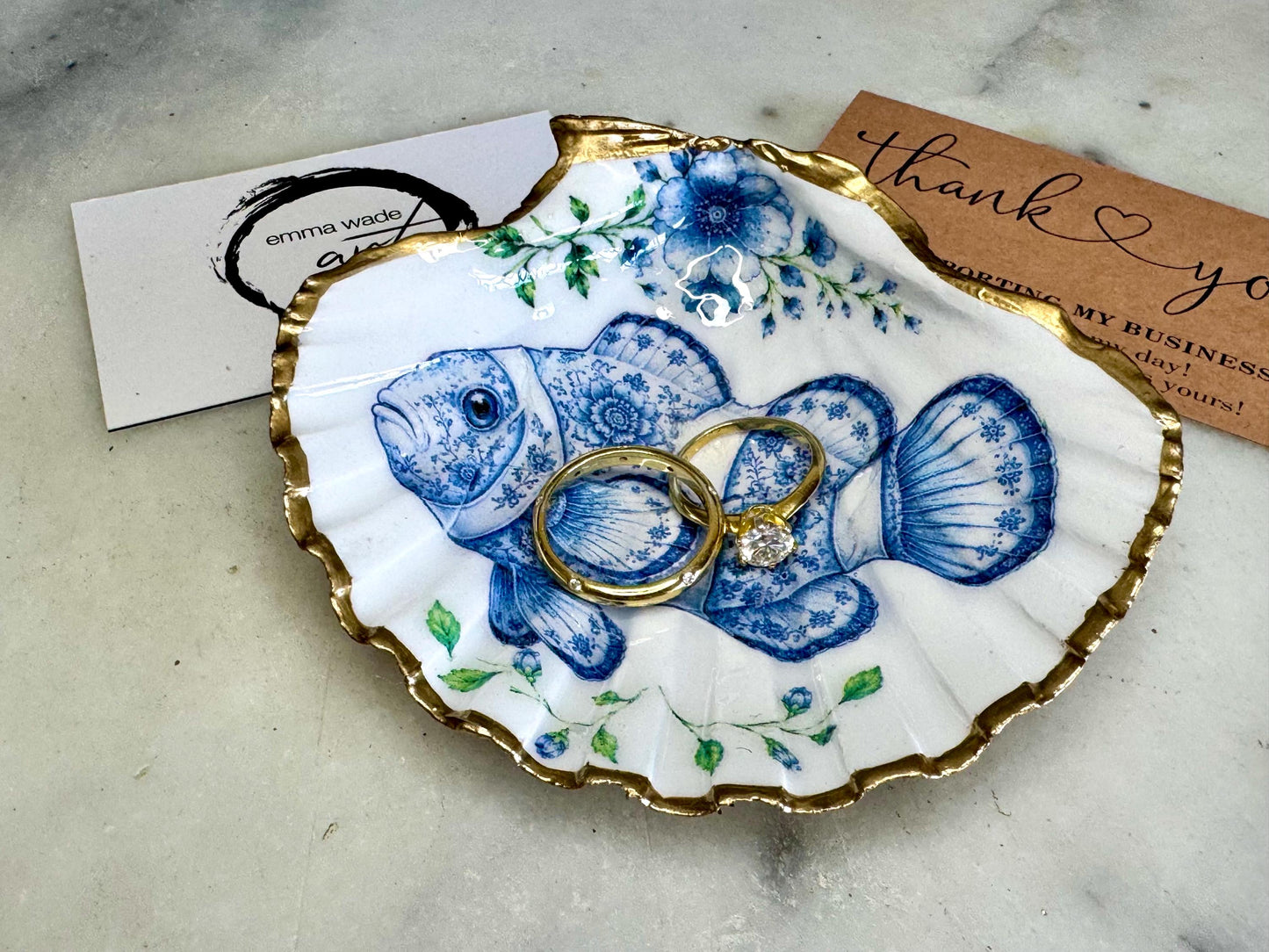 Clownfish scallop shell trinket dish featuring an original illustrated Delft Blue design by Emma Wade ART. Natural scallop shell finished with gold leaf or silver leaf edging and a crystal-clear glossy resin coating. Coastal jewellery tray, ring holder and ocean-inspired gift for fish and sea lovers, beach house décor, weddings, bridesmaids and nautical homes.