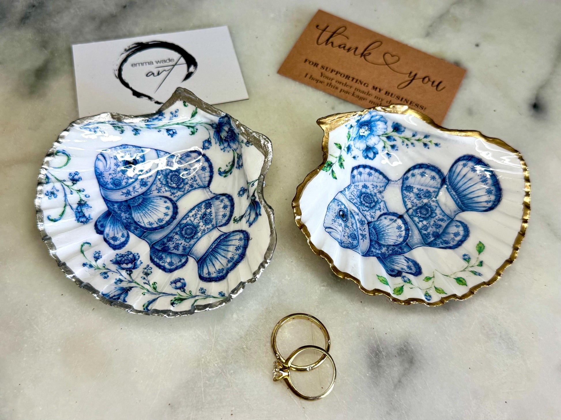 Clownfish scallop shell trinket dish featuring an original illustrated Delft Blue design by Emma Wade ART. Natural scallop shell finished with gold leaf or silver leaf edging and a crystal-clear glossy resin coating. Coastal jewellery tray, Floral ring holder and ocean-inspired gift for fish and sea lovers, beach house décor, weddings, bridesmaids and nautical homes.