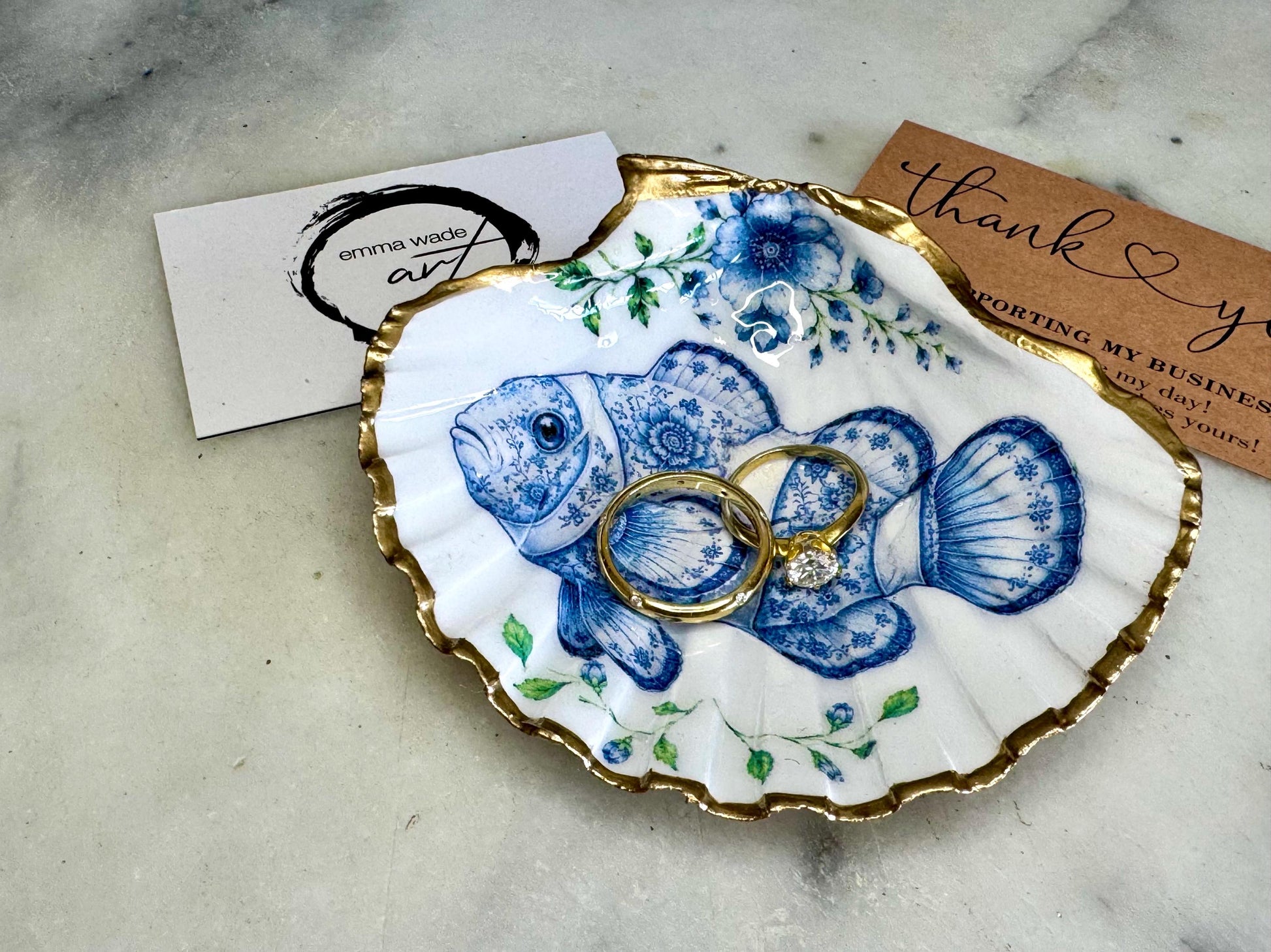 Clownfish scallop shell trinket dish featuring an original illustrated Delft Blue design by Emma Wade ART. Natural scallop shell finished with gold leaf or silver leaf edging and a crystal-clear glossy resin coating. Coastal jewellery tray, Floral ring holder and ocean-inspired gift for fish and sea lovers, beach house décor, weddings, bridesmaids and nautical homes.