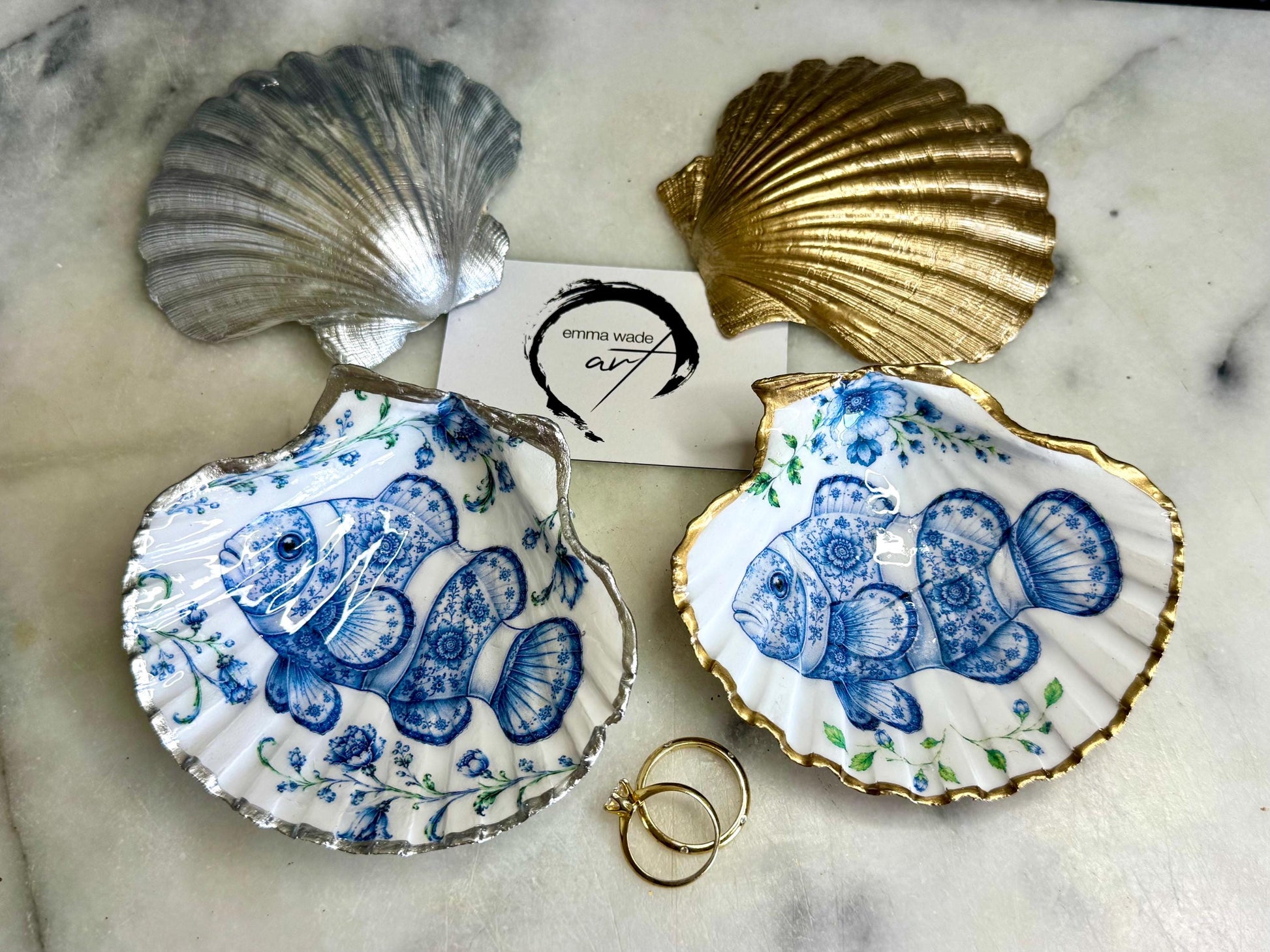 Clownfish scallop shell trinket dish featuring an original illustrated Delft Blue design by Emma Wade ART. Natural scallop shell finished with gold leaf or silver leaf edging and a crystal-clear glossy resin coating. Coastal jewellery tray, Floral ring holder and ocean-inspired gift for fish and sea lovers, beach house décor, weddings, bridesmaids and nautical homes.
