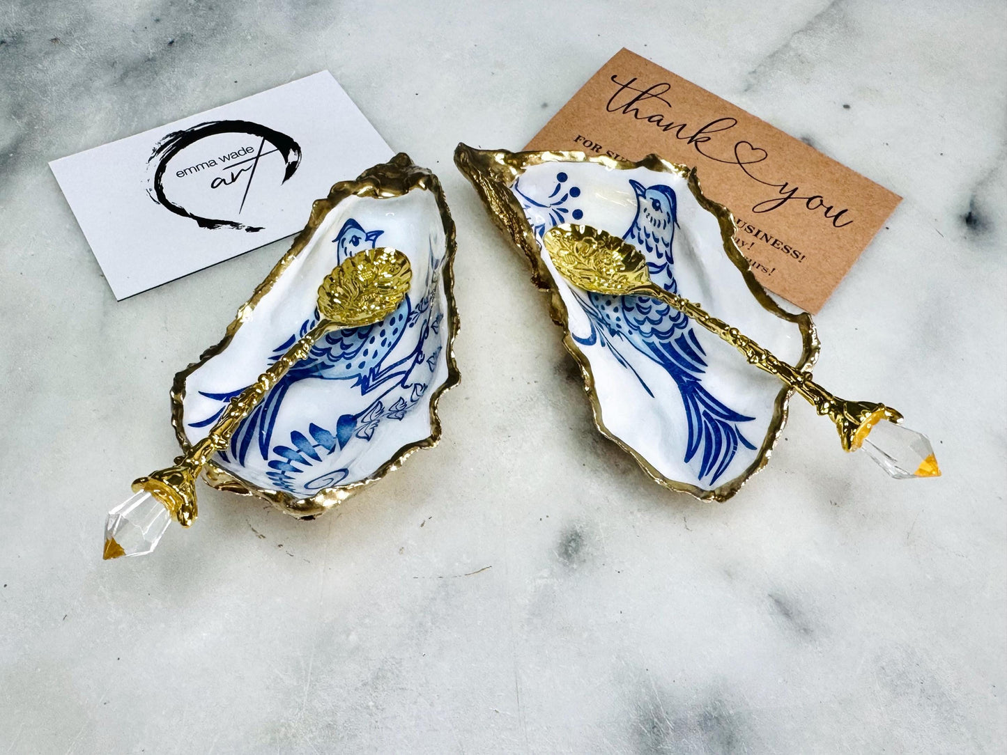 Handmade blue bird oyster shell salt and pepper pinch pot set crafted from natural Dorset oyster shells with glossy pearlescent interiors, blue porcelain style bird artwork and shimmering liquid gold leaf edging. Luxury coastal cruet dishes sealed with gloss resin and styled with optional gold spoons. Elegant seaside dining decor for beach house kitchens, dinner parties, weddings, anniversaries and bird lovers. Artisan shell tableware handmade in the UK with coastal blue and white styling.