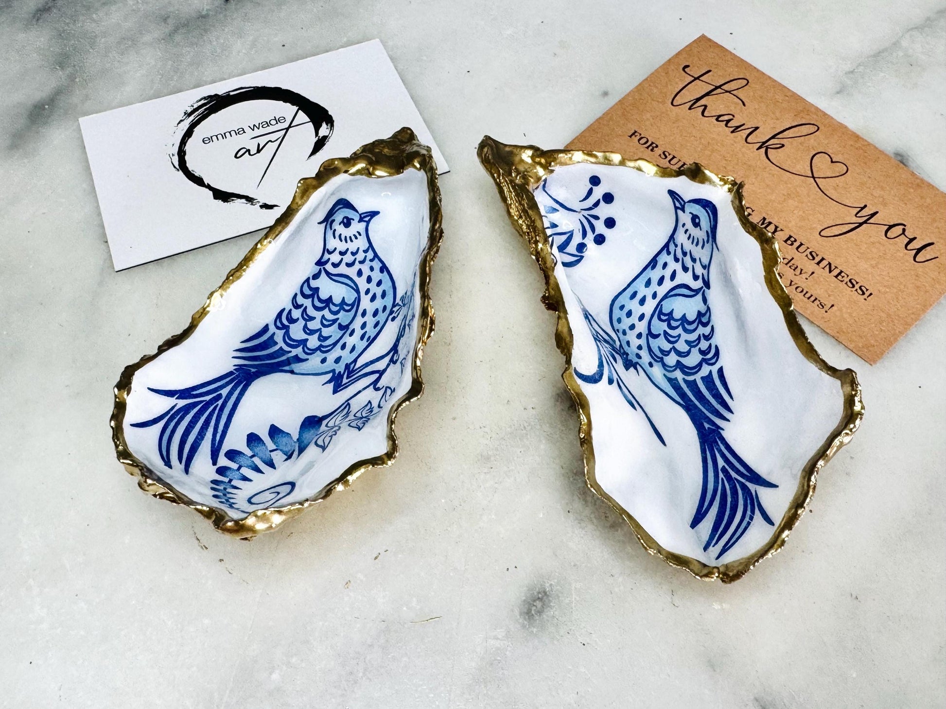 Handmade blue bird oyster shell salt and pepper pinch pot set crafted from natural Dorset oyster shells with glossy pearlescent interiors, blue porcelain style bird artwork and shimmering liquid gold leaf edging. Luxury coastal cruet dishes sealed with gloss resin and styled with optional gold spoons. Elegant seaside dining decor for beach house kitchens, dinner parties, weddings, anniversaries and bird lovers. Artisan shell tableware handmade in the UK with coastal blue and white styling.