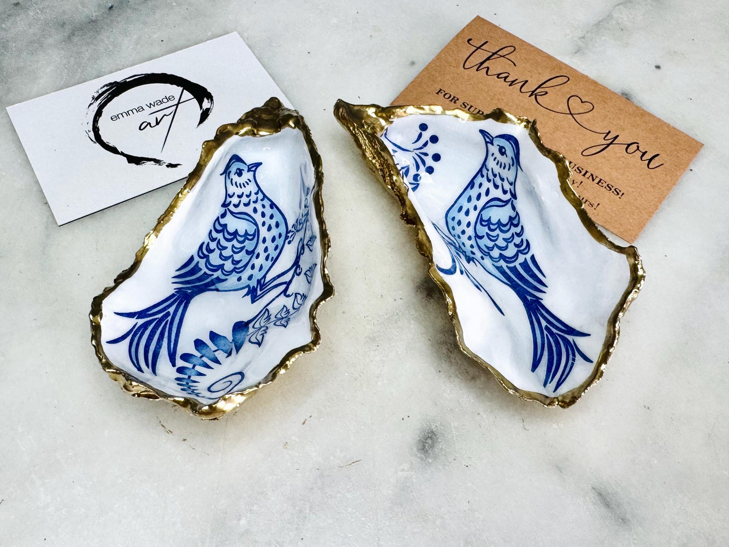 Handmade blue bird oyster shell salt and pepper pinch pot set crafted from natural Dorset oyster shells with glossy pearlescent interiors, blue porcelain style bird artwork and shimmering liquid gold leaf edging. Luxury coastal cruet dishes sealed with gloss resin and styled with optional gold spoons. Elegant seaside dining decor for beach house kitchens, dinner parties, weddings, anniversaries and bird lovers. Artisan shell tableware handmade in the UK with coastal blue and white styling.