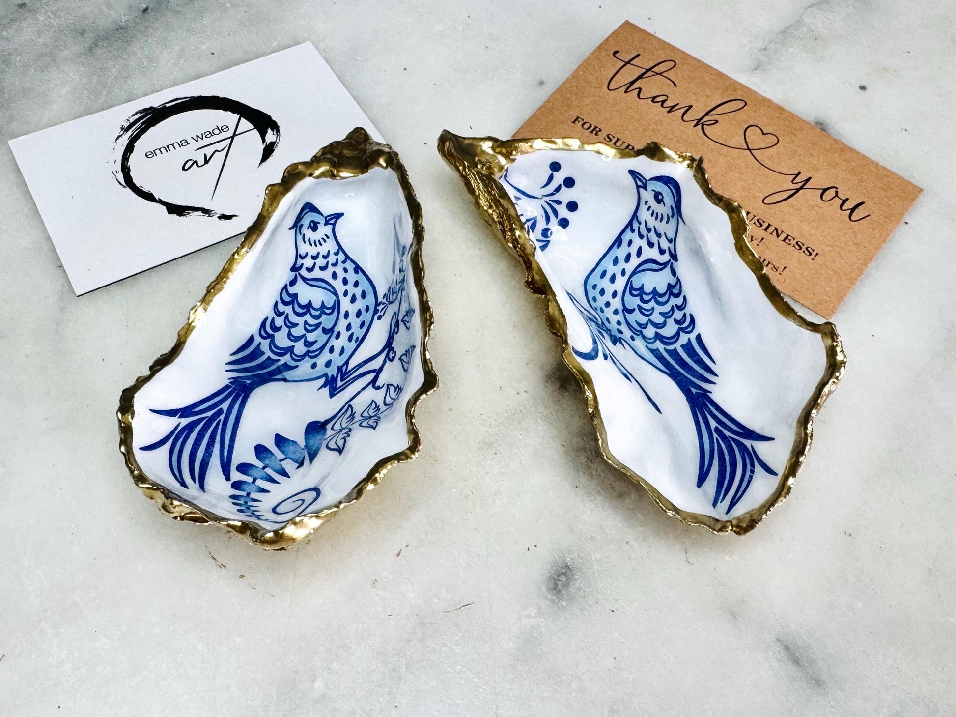 Handmade blue bird oyster shell salt and pepper pinch pot set crafted from natural Dorset oyster shells with glossy pearlescent interiors, blue porcelain style bird artwork and shimmering liquid gold leaf edging. Luxury coastal cruet dishes sealed with gloss resin and styled with optional gold spoons. Elegant seaside dining decor for beach house kitchens, dinner parties, weddings, anniversaries and bird lovers. Artisan shell tableware handmade in the UK with coastal blue and white styling.