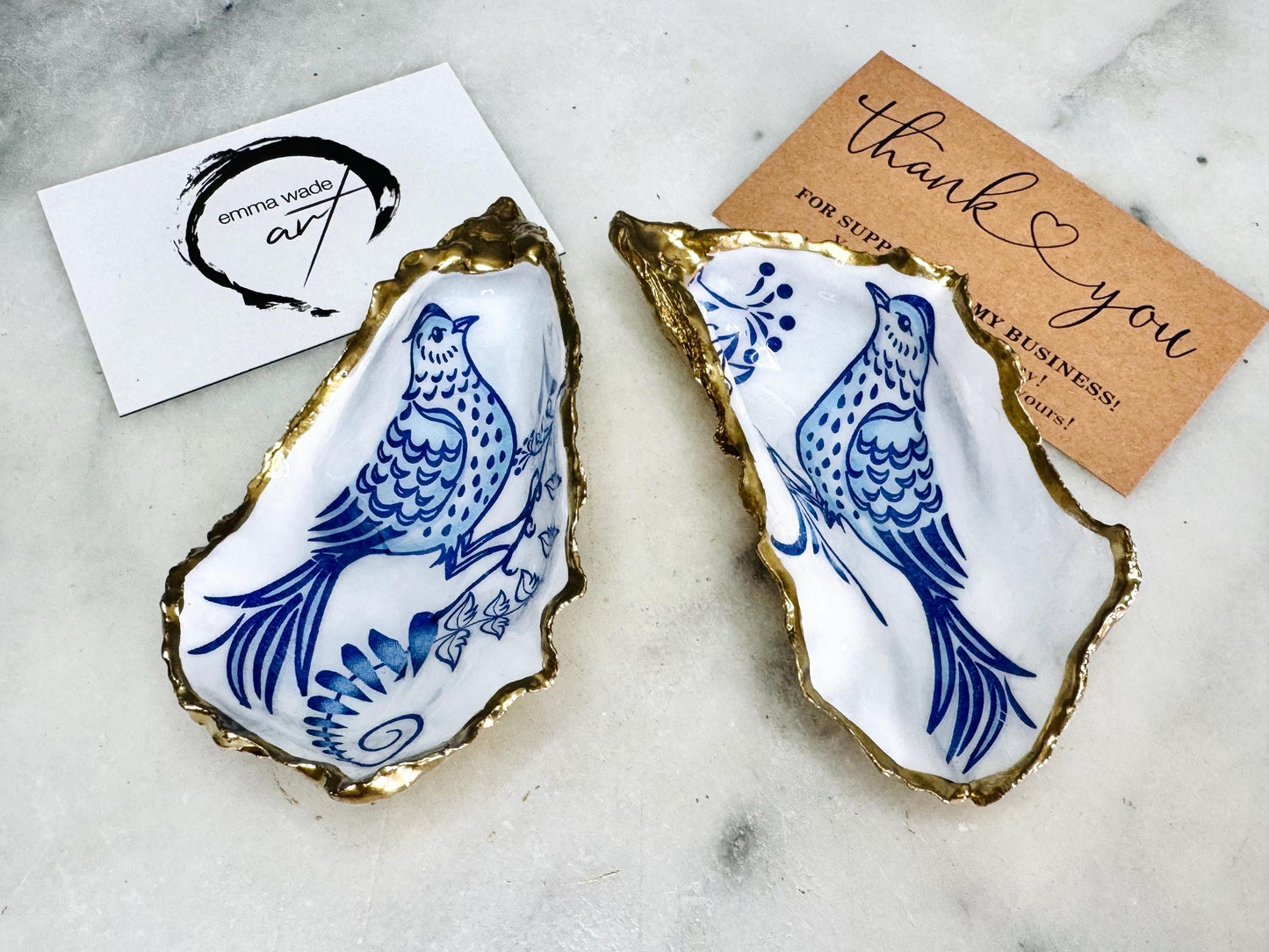 Handmade blue bird oyster shell salt and pepper pinch pot set crafted from natural Dorset oyster shells with glossy pearlescent interiors, blue porcelain style bird artwork and shimmering liquid gold leaf edging. Luxury coastal cruet dishes sealed with gloss resin and styled with optional gold spoons. Elegant seaside dining decor for beach house kitchens, dinner parties, weddings, anniversaries and bird lovers. Artisan shell tableware handmade in the UK with coastal blue and white styling.