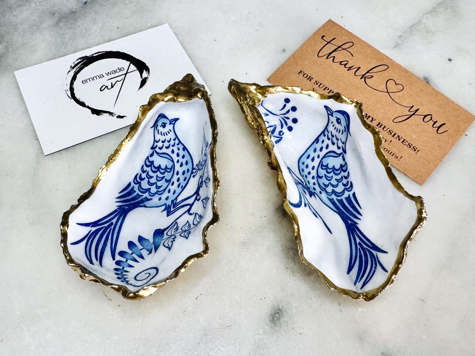 Handmade blue bird oyster shell salt and pepper pinch pot set crafted from natural Dorset oyster shells with glossy pearlescent interiors, blue porcelain style bird artwork and shimmering liquid gold leaf edging. Luxury coastal cruet dishes sealed with gloss resin and styled with optional gold spoons. Elegant seaside dining decor for beach house kitchens, dinner parties, weddings, anniversaries and bird lovers. Artisan shell tableware handmade in the UK with coastal blue and white styling.