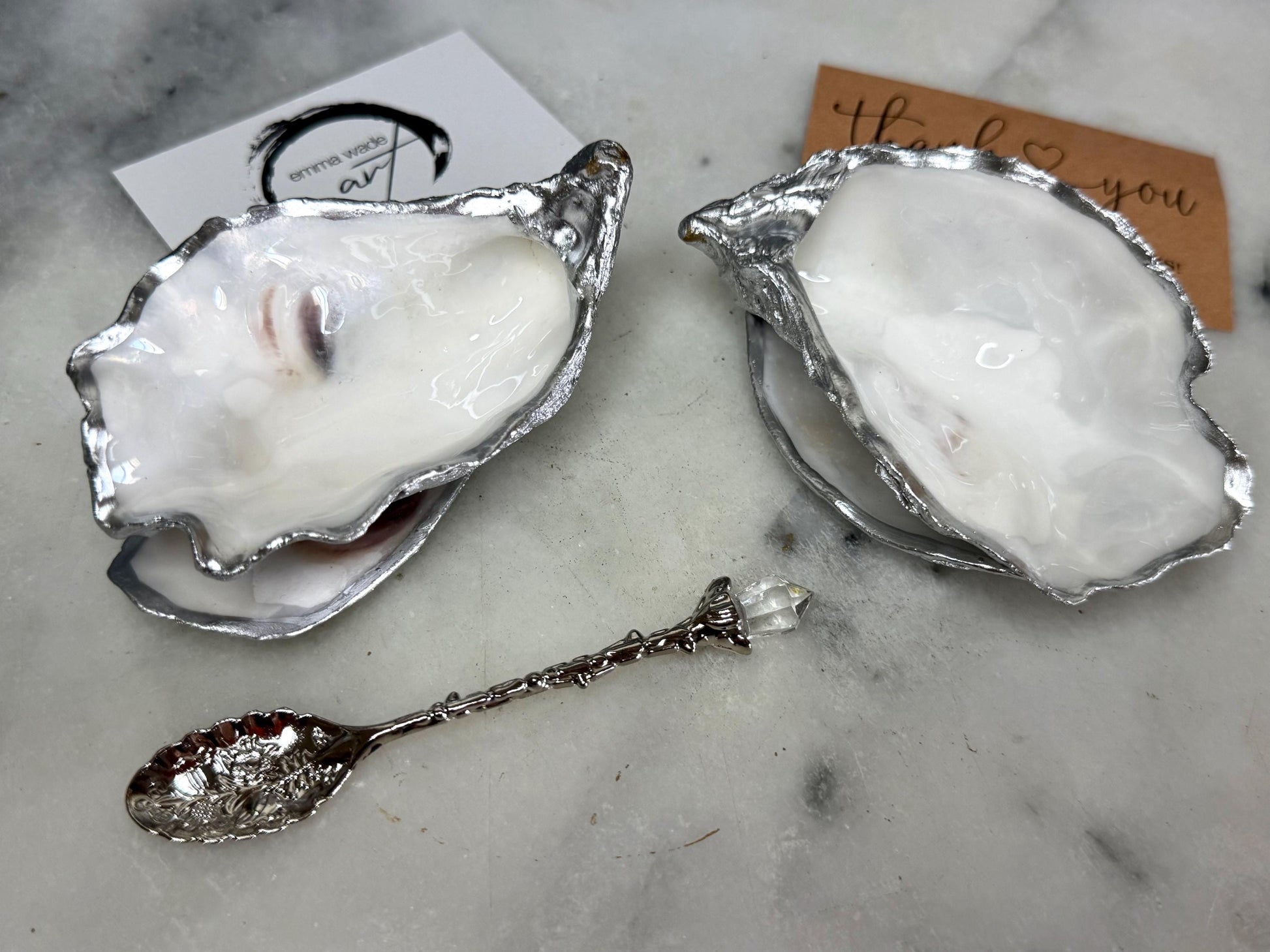 Handmade pearl oyster shell salt and pepper pinch pots with silver leaf accents and optional crystal spoons. Coastal tableware set made from natural Dorset oyster shells, polished to a natural white pearl finish and sealed with food-safe glossy resin. Elegant shell salt dishes photographed on a light background, showing two domed shells with matching bases, ideal for serving salt, pepper or spices at stylish dinner tables and special occasions.