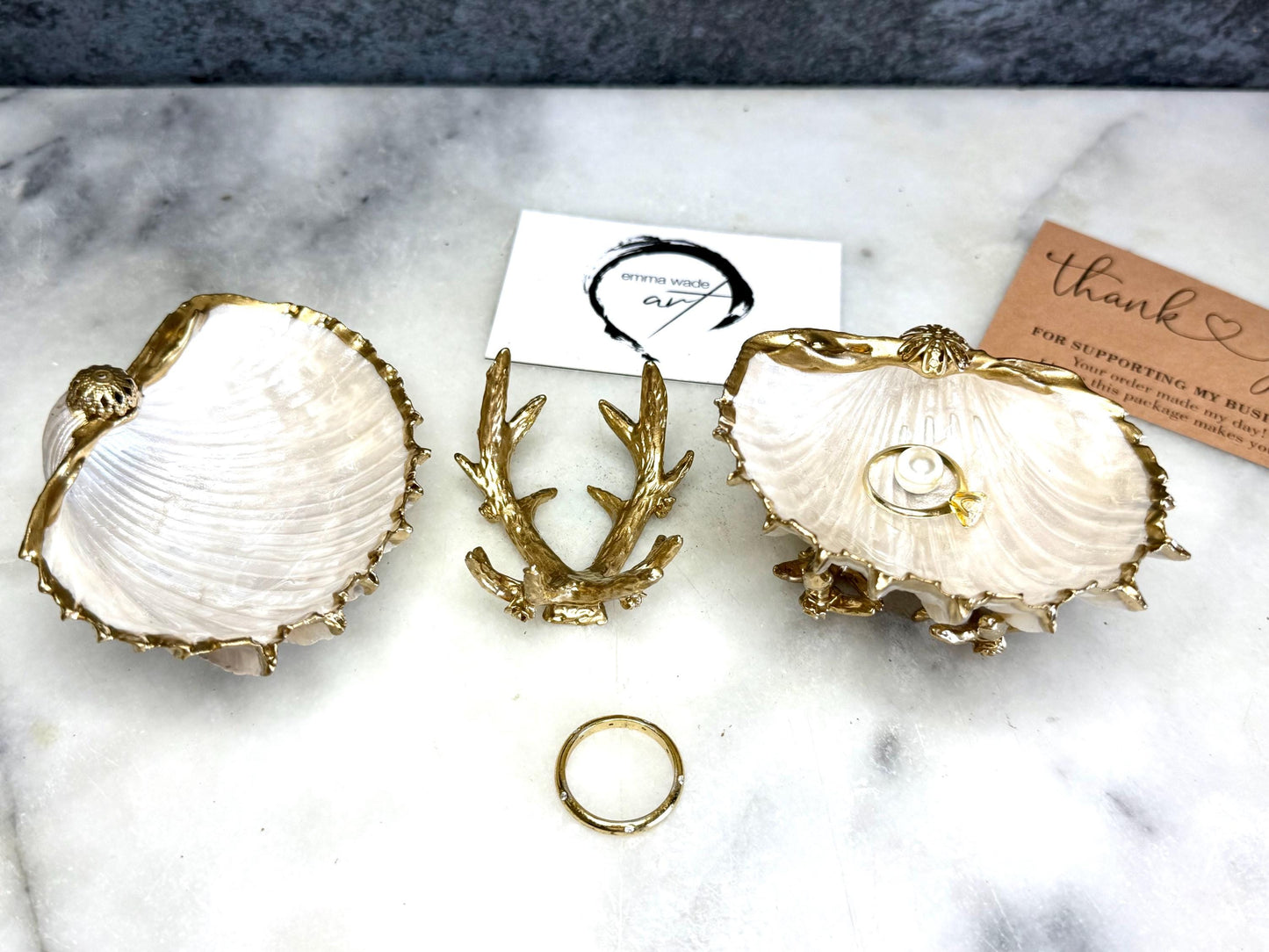 Luxury natural Spiny Cockle shell proposal and wedding ring dish on an ornate gold metal stand, available with or without an inset Swarovski pearl ring holder. Pearlescent shell approximately 8–9cm wide with a hand-gilded liquid gold leaf rim, delicate gold embellishments and crystal-clear resin finish. Handmade luxury jewellery holder, engagement ring dish, bridal keepsake and coastal decor by Emma Wade ART.