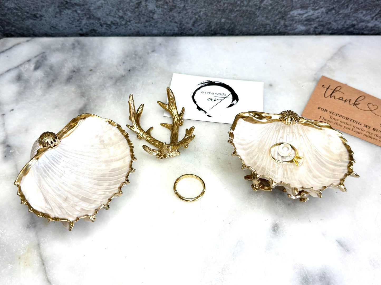 Luxury natural Spiny Cockle shell proposal and wedding ring dish on an ornate gold metal stand, available with or without an inset Swarovski pearl ring holder. Pearlescent shell approximately 8–9cm wide with a hand-gilded liquid gold leaf rim, delicate gold embellishments and crystal-clear resin finish. Handmade luxury jewellery holder, engagement ring dish, bridal keepsake and coastal decor by Emma Wade ART.