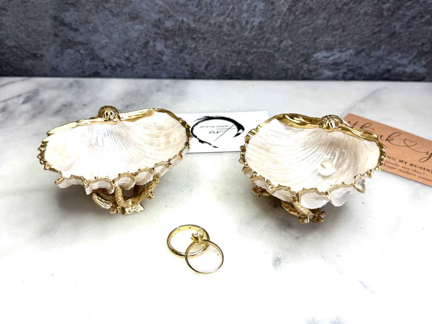 Luxury natural Spiny Cockle shell proposal and wedding ring dish on an ornate gold metal stand, available with or without an inset Swarovski pearl ring holder. Pearlescent shell approximately 8–9cm wide with a hand-gilded liquid gold leaf rim, delicate gold embellishments and crystal-clear resin finish. Handmade luxury jewellery holder, engagement ring dish, bridal keepsake and coastal decor by Emma Wade ART.