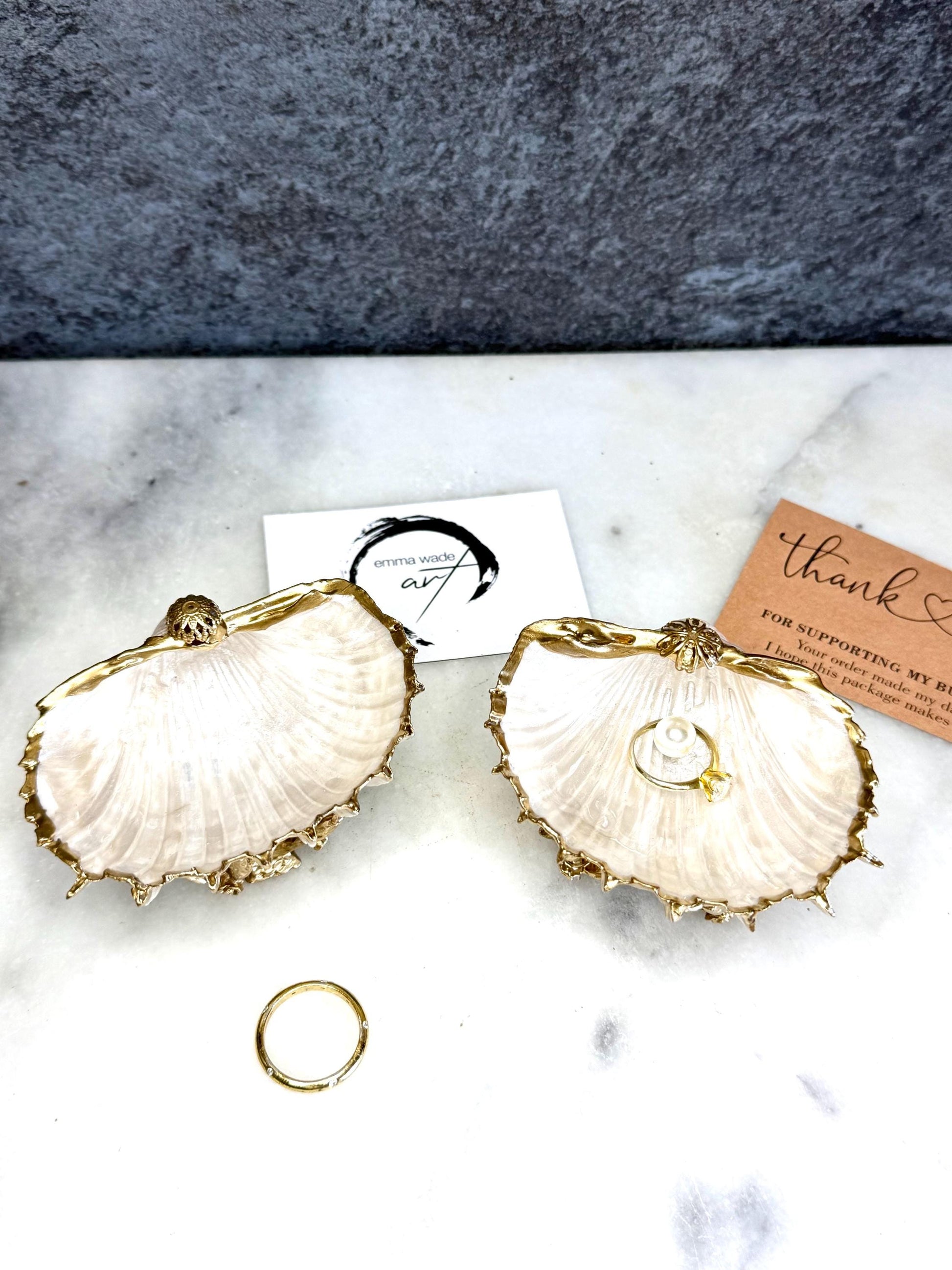 Luxury natural Spiny Cockle shell proposal and wedding ring dish on an ornate gold metal stand, available with or without an inset Swarovski pearl ring holder. Pearlescent shell approximately 8–9cm wide with a hand-gilded liquid gold leaf rim, delicate gold embellishments and crystal-clear resin finish. Handmade luxury jewellery holder, engagement ring dish, bridal keepsake and coastal decor by Emma Wade ART.