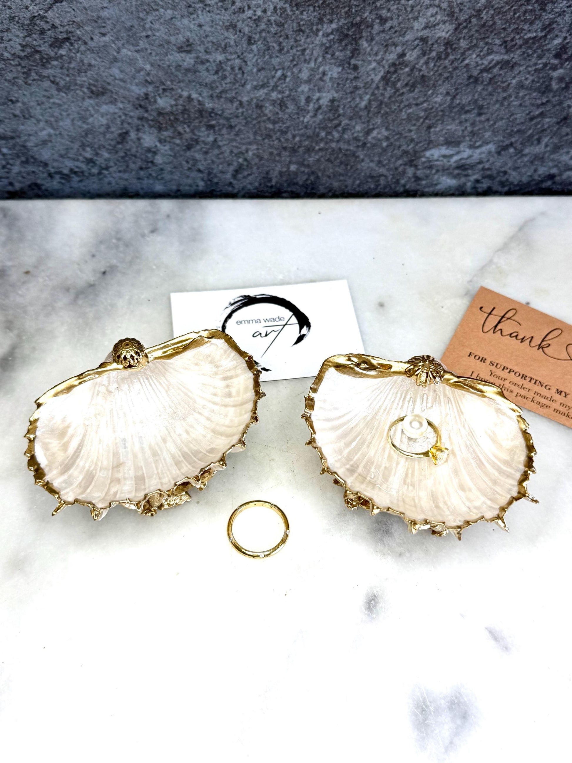 Luxury natural Spiny Cockle shell proposal and wedding ring dish on an ornate gold metal stand, available with or without an inset Swarovski pearl ring holder. Pearlescent shell approximately 8–9cm wide with a hand-gilded liquid gold leaf rim, delicate gold embellishments and crystal-clear resin finish. Handmade luxury jewellery holder, engagement ring dish, bridal keepsake and coastal decor by Emma Wade ART.