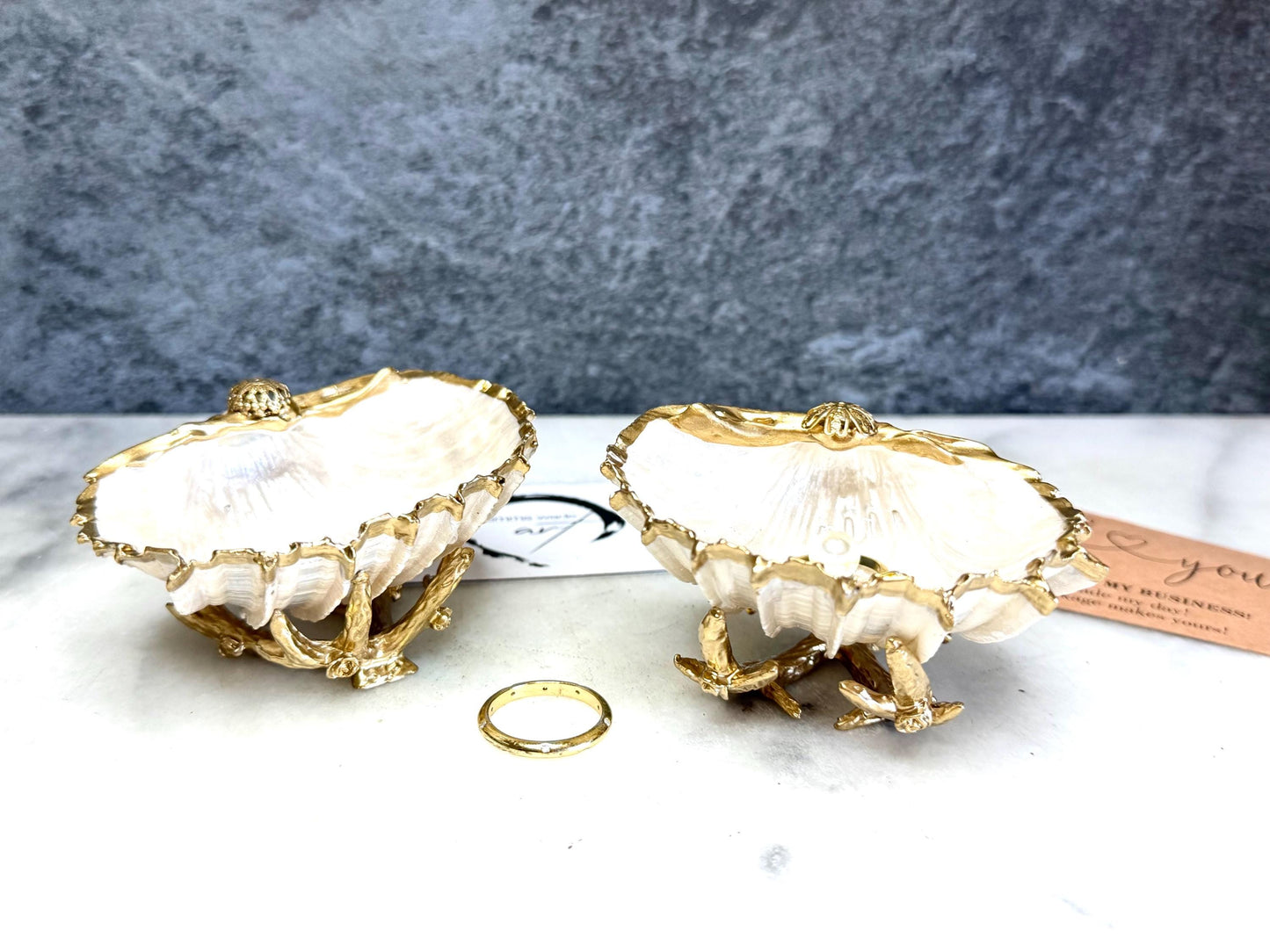 Luxury natural Spiny Cockle shell proposal and wedding ring dish on an ornate gold metal stand, available with or without an inset Swarovski pearl ring holder. Pearlescent shell approximately 8–9cm wide with a hand-gilded liquid gold leaf rim, delicate gold embellishments and crystal-clear resin finish. Handmade luxury jewellery holder, engagement ring dish, bridal keepsake and coastal decor by Emma Wade ART.
