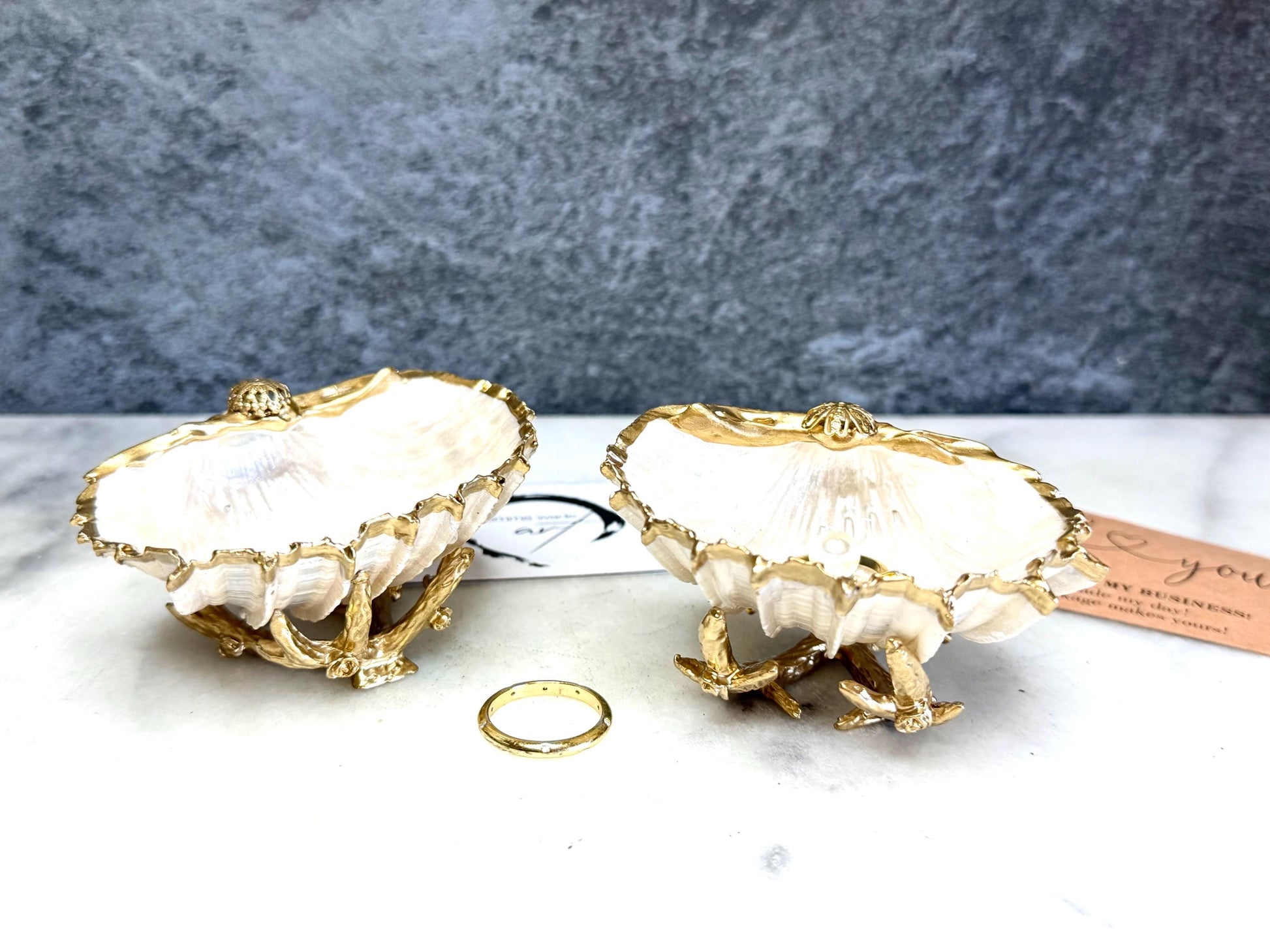 Luxury natural Spiny Cockle shell proposal and wedding ring dish on an ornate gold metal stand, available with or without an inset Swarovski pearl ring holder. Pearlescent shell approximately 8–9cm wide with a hand-gilded liquid gold leaf rim, delicate gold embellishments and crystal-clear resin finish. Handmade luxury jewellery holder, engagement ring dish, bridal keepsake and coastal decor by Emma Wade ART.