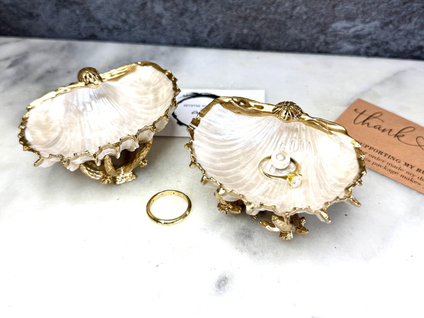 Luxury natural Spiny Cockle shell proposal and wedding ring dish on an ornate gold metal stand, available with or without an inset Swarovski pearl ring holder. Pearlescent shell approximately 8–9cm wide with a hand-gilded liquid gold leaf rim, delicate gold embellishments and crystal-clear resin finish. Handmade luxury jewellery holder, engagement ring dish, bridal keepsake and coastal decor by Emma Wade ART.