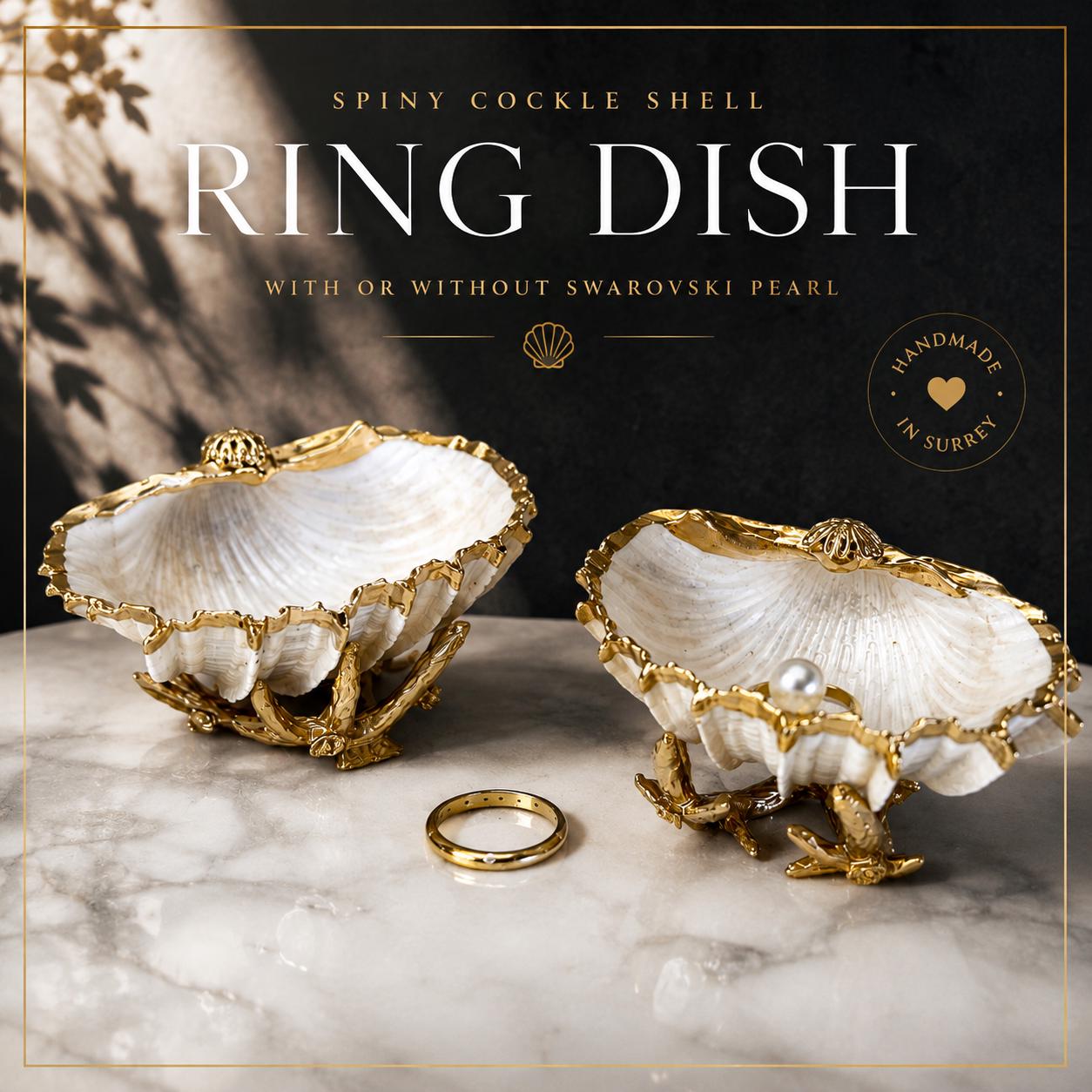 Luxury natural Spiny Cockle shell proposal and wedding ring dish on an ornate gold metal stand, available with or without an inset Swarovski pearl ring holder. Pearlescent shell approximately 8–9cm wide with a hand-gilded liquid gold leaf rim, delicate gold embellishments and crystal-clear resin finish. Handmade luxury jewellery holder, engagement ring dish, bridal keepsake and coastal decor by Emma Wade ART.