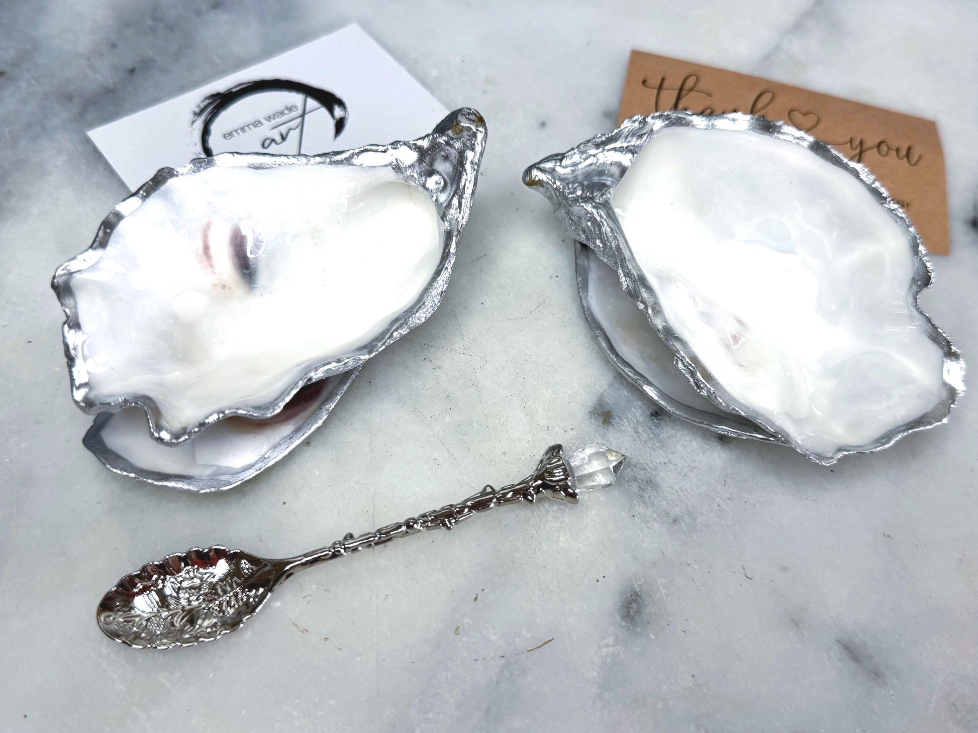 Handmade pearl oyster shell salt and pepper pinch pots with silver leaf accents and optional crystal spoons. Coastal tableware set made from natural Dorset oyster shells, polished to a natural white pearl finish and sealed with food-safe glossy resin. Elegant shell salt dishes photographed on a light background, showing two domed shells with matching bases, ideal for serving salt, pepper or spices at stylish dinner tables and special occasions.