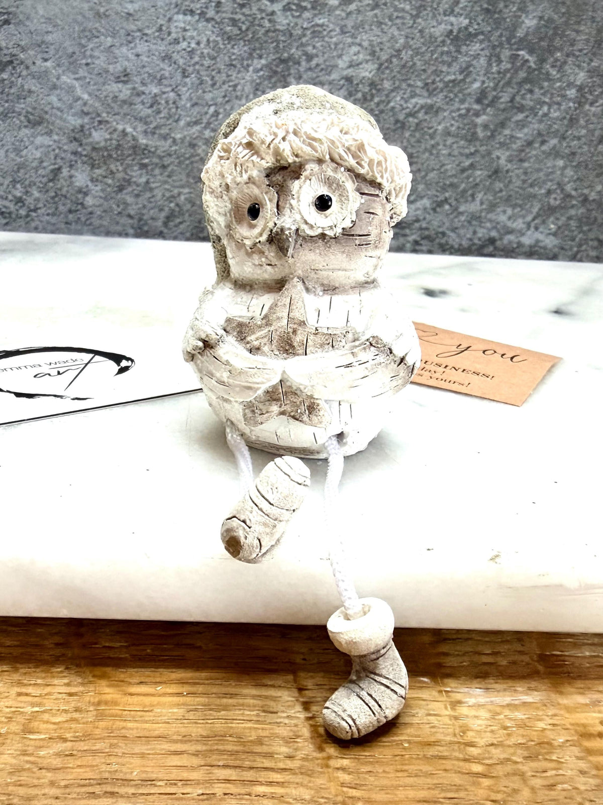 Set of three woodland Christmas owl shelf sitter decorations in soft white, grey and natural tones, featuring winter hats, scarves and festive details. Moulded resin owl ornaments with subtle glitter accents and dangling cord legs with little boots, designed to sit on a shelf, mantelpiece or windowsill. Festive woodland Christmas décor and owl lover gift.