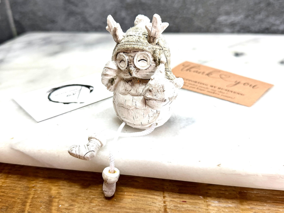 Set of three woodland Christmas owl shelf sitter decorations in soft white, grey and natural tones, featuring winter hats, scarves and festive details. Moulded resin owl ornaments with subtle glitter accents and dangling cord legs with little boots, designed to sit on a shelf, mantelpiece or windowsill. Festive woodland Christmas décor and owl lover gift.