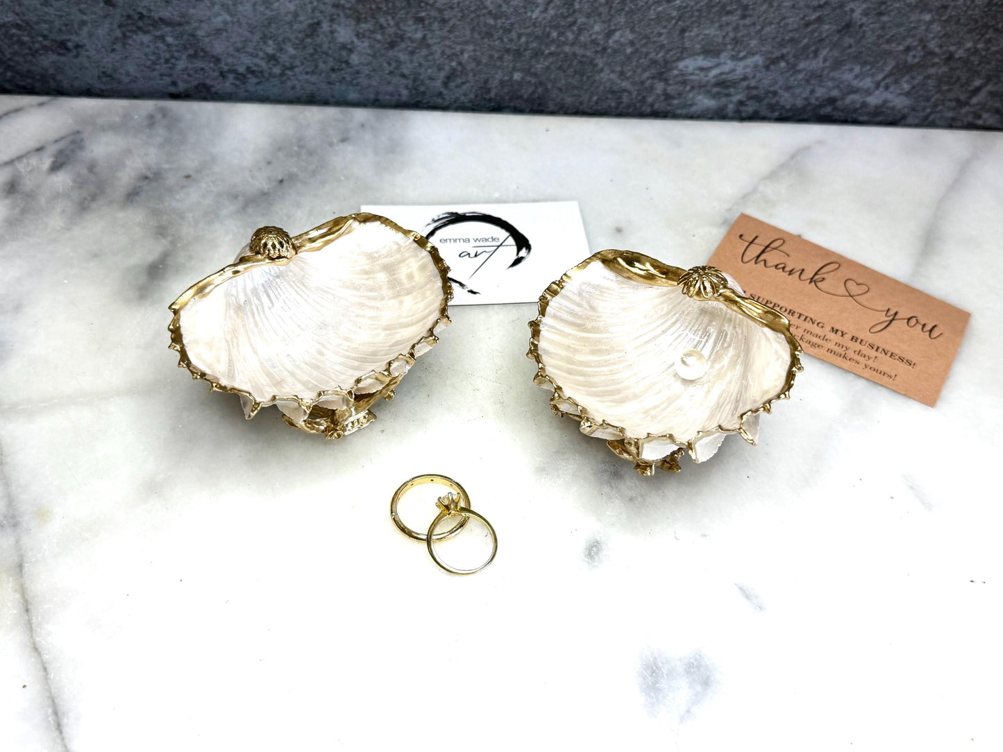 Luxury natural Spiny Cockle shell proposal and wedding ring dish on an ornate gold metal stand, available with or without an inset Swarovski pearl ring holder. Pearlescent shell approximately 8–9cm wide with a hand-gilded liquid gold leaf rim, delicate gold embellishments and crystal-clear resin finish. Handmade luxury jewellery holder, engagement ring dish, bridal keepsake and coastal decor by Emma Wade ART.