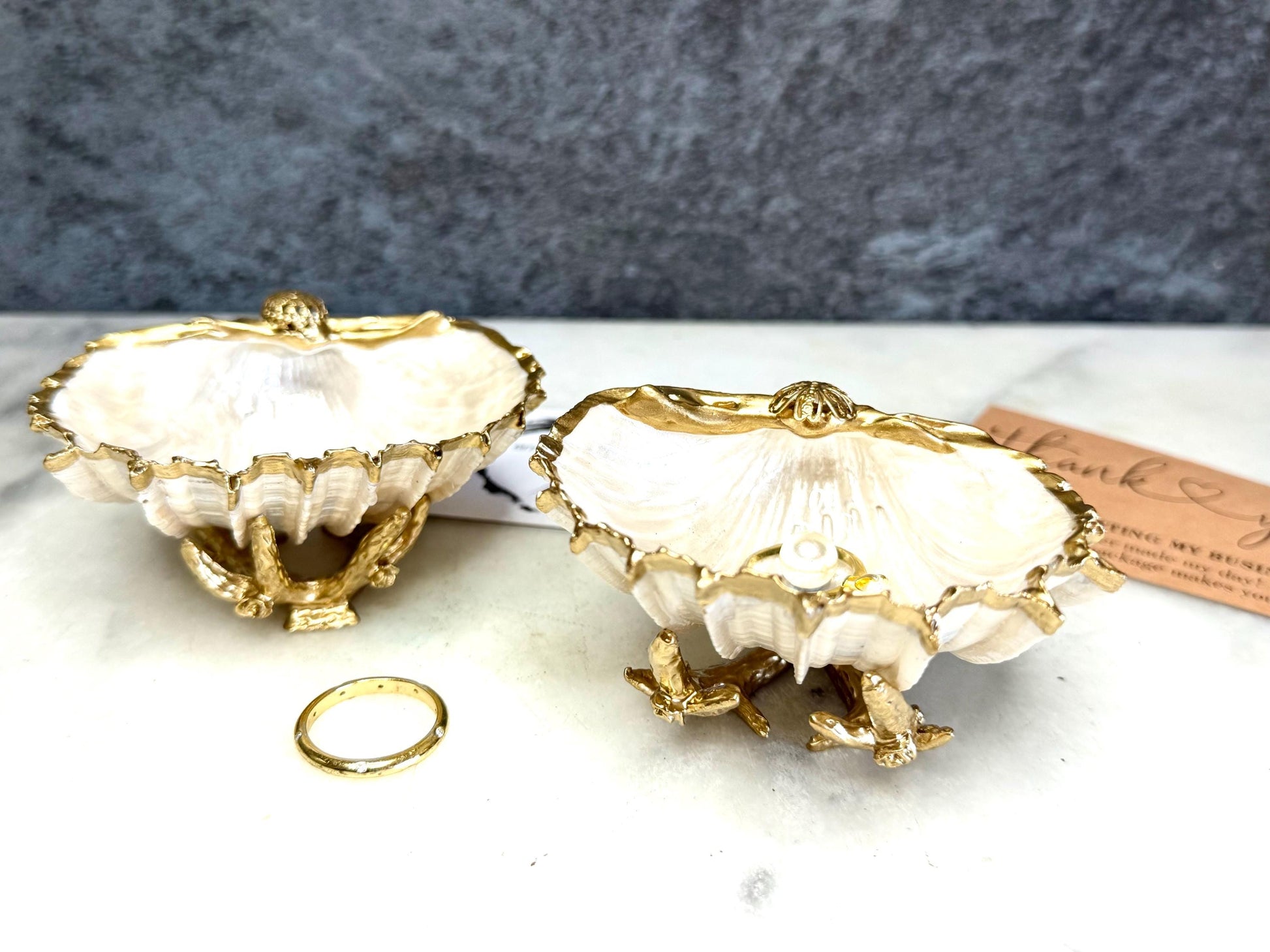 Luxury natural Spiny Cockle shell proposal and wedding ring dish on an ornate gold metal stand, available with or without an inset Swarovski pearl ring holder. Pearlescent shell approximately 8–9cm wide with a hand-gilded liquid gold leaf rim, delicate gold embellishments and crystal-clear resin finish. Handmade luxury jewellery holder, engagement ring dish, bridal keepsake and coastal decor by Emma Wade ART.
