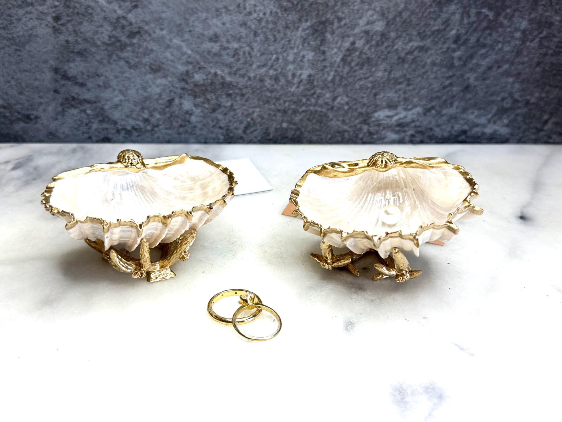 Luxury natural Spiny Cockle shell proposal and wedding ring dish on an ornate gold metal stand, available with or without an inset Swarovski pearl ring holder. Pearlescent shell approximately 8–9cm wide with a hand-gilded liquid gold leaf rim, delicate gold embellishments and crystal-clear resin finish. Handmade luxury jewellery holder, engagement ring dish, bridal keepsake and coastal decor by Emma Wade ART.