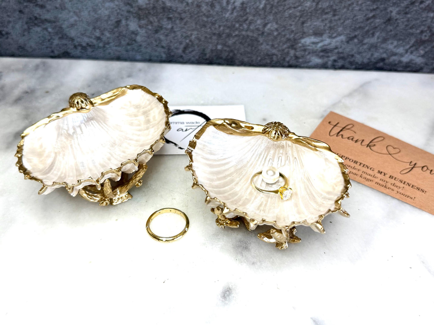 Luxury natural Spiny Cockle shell proposal and wedding ring dish on an ornate gold metal stand, available with or without an inset Swarovski pearl ring holder. Pearlescent shell approximately 8–9cm wide with a hand-gilded liquid gold leaf rim, delicate gold embellishments and crystal-clear resin finish. Handmade luxury jewellery holder, engagement ring dish, bridal keepsake and coastal decor by Emma Wade ART.