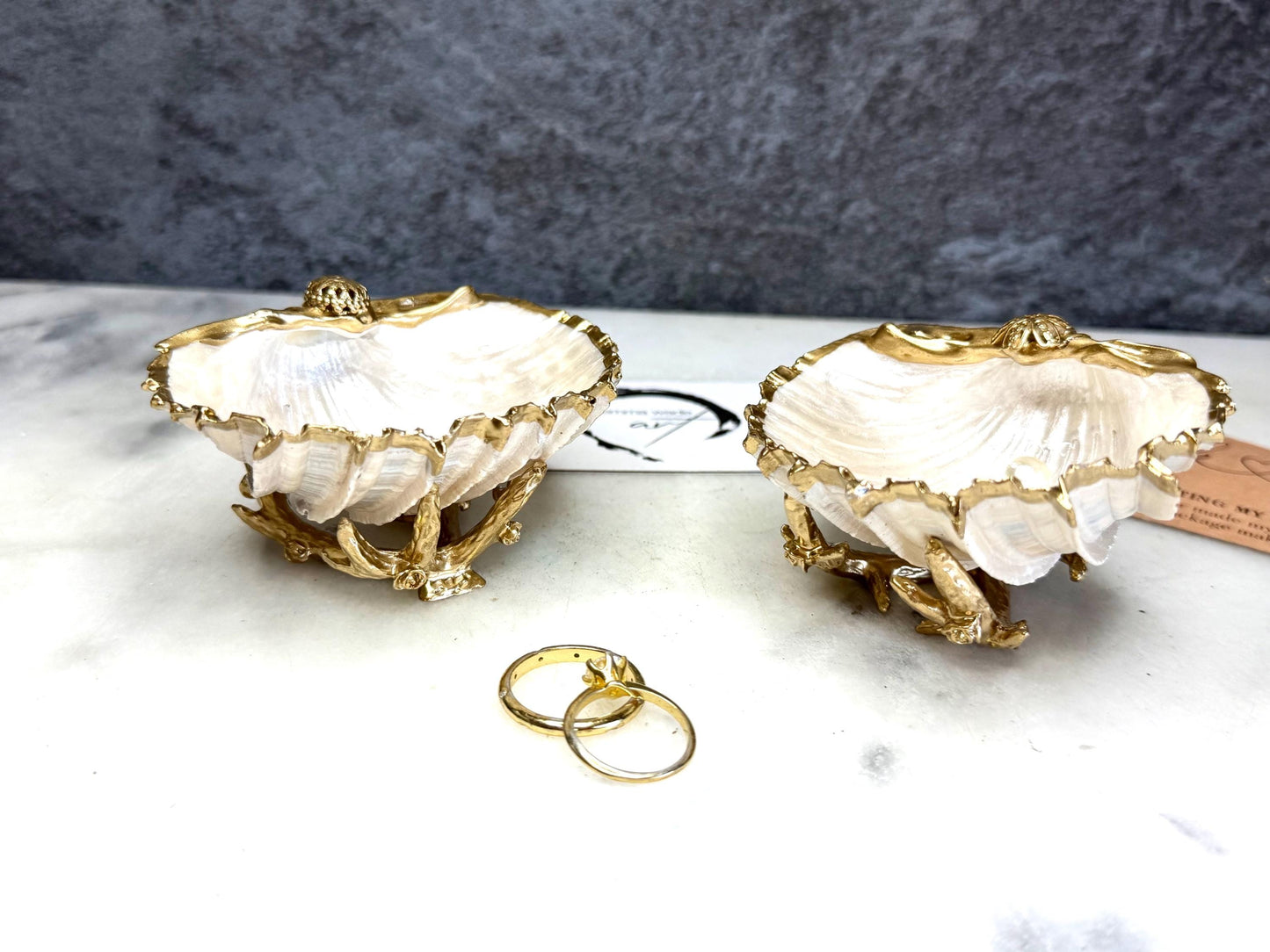 Luxury natural Spiny Cockle shell proposal and wedding ring dish on an ornate gold metal stand, available with or without an inset Swarovski pearl ring holder. Pearlescent shell approximately 8–9cm wide with a hand-gilded liquid gold leaf rim, delicate gold embellishments and crystal-clear resin finish. Handmade luxury jewellery holder, engagement ring dish, bridal keepsake and coastal decor by Emma Wade ART.