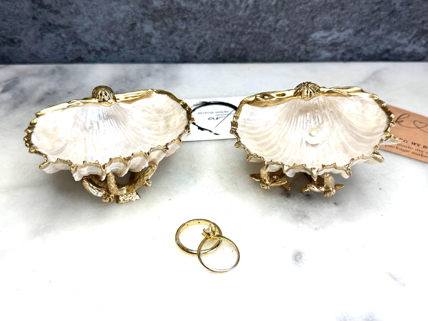 Luxury natural Spiny Cockle shell proposal and wedding ring dish on an ornate gold metal stand, available with or without an inset Swarovski pearl ring holder. Pearlescent shell approximately 8–9cm wide with a hand-gilded liquid gold leaf rim, delicate gold embellishments and crystal-clear resin finish. Handmade luxury jewellery holder, engagement ring dish, bridal keepsake and coastal decor by Emma Wade ART.