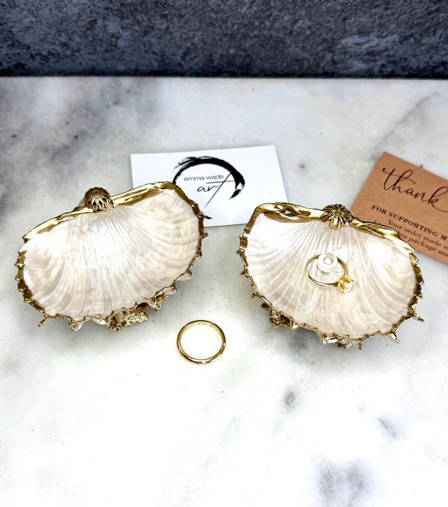 Luxury natural Spiny Cockle shell proposal and wedding ring dish on an ornate gold metal stand, available with or without an inset Swarovski pearl ring holder. Pearlescent shell approximately 8–9cm wide with a hand-gilded liquid gold leaf rim, delicate gold embellishments and crystal-clear resin finish. Handmade luxury jewellery holder, engagement ring dish, bridal keepsake and coastal decor by Emma Wade ART.