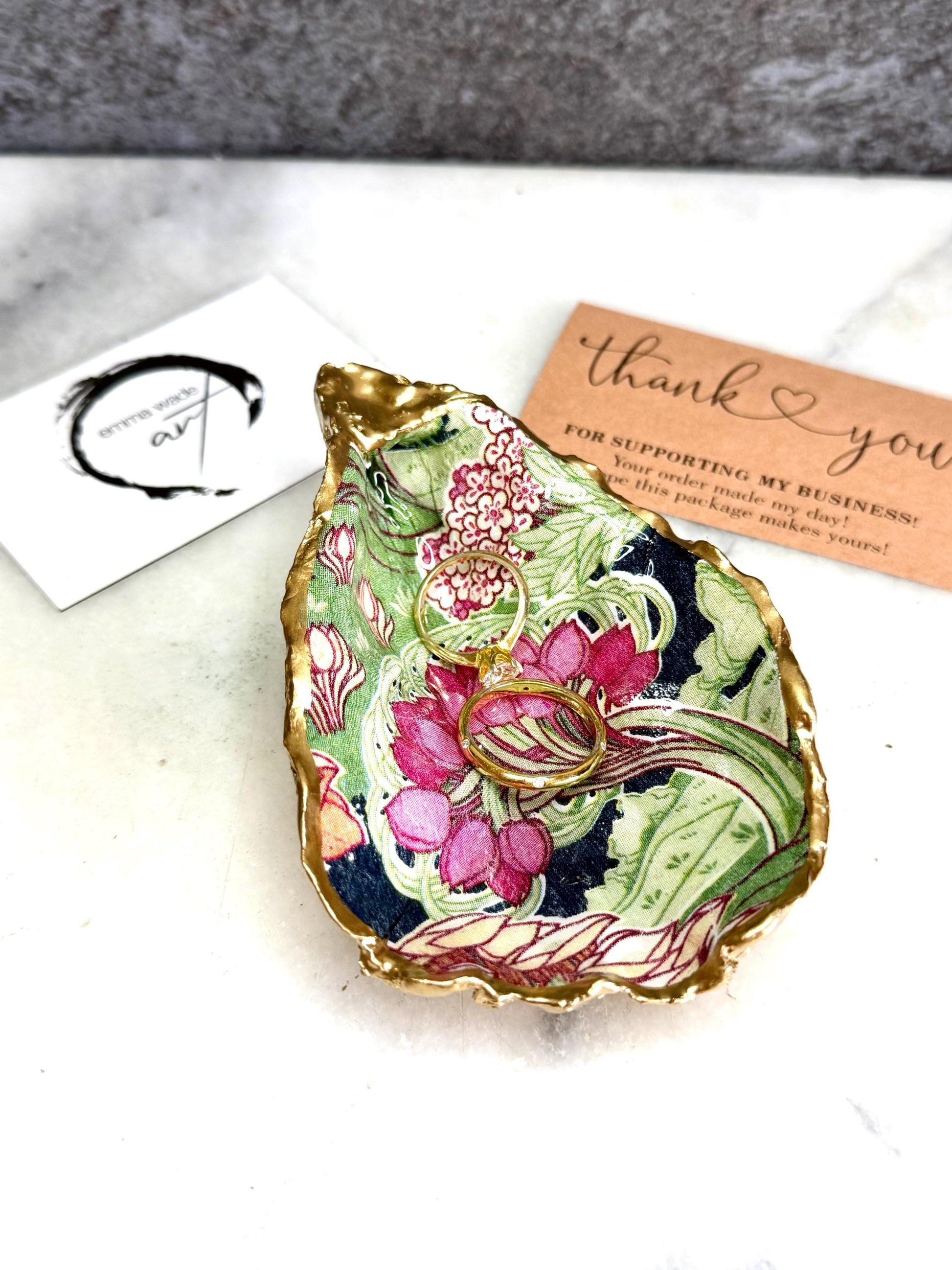 Handcrafted V&A Museum Swirling Trees shell dish collection featuring large and small scallop shells and oyster shells decorated with flowing botanical artwork, pink water lilies and rich green foliage. Each natural Dorset shell is hand-gilded with real liquid gold leaf and sealed with crystal-clear resin. Luxury coastal decor, jewellery dishes, ring holders and trinket trays. Available individually or as a coordinated set of four shells.