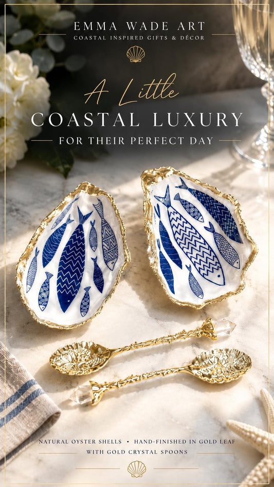 Pair of handmade Dorset oyster shell salt and pepper pinch pots decorated with elegant blue and white fish artwork, finished with hand applied liquid gold leaf edging and sealed in glossy food-safe resin. Coastal shell cruet dishes styled with optional gold crystal spoons on a marble background. Luxury nautical kitchen decor inspired by the sea, perfect for beach house dining, dinner parties, weddings, anniversaries, and coastal home gifts.