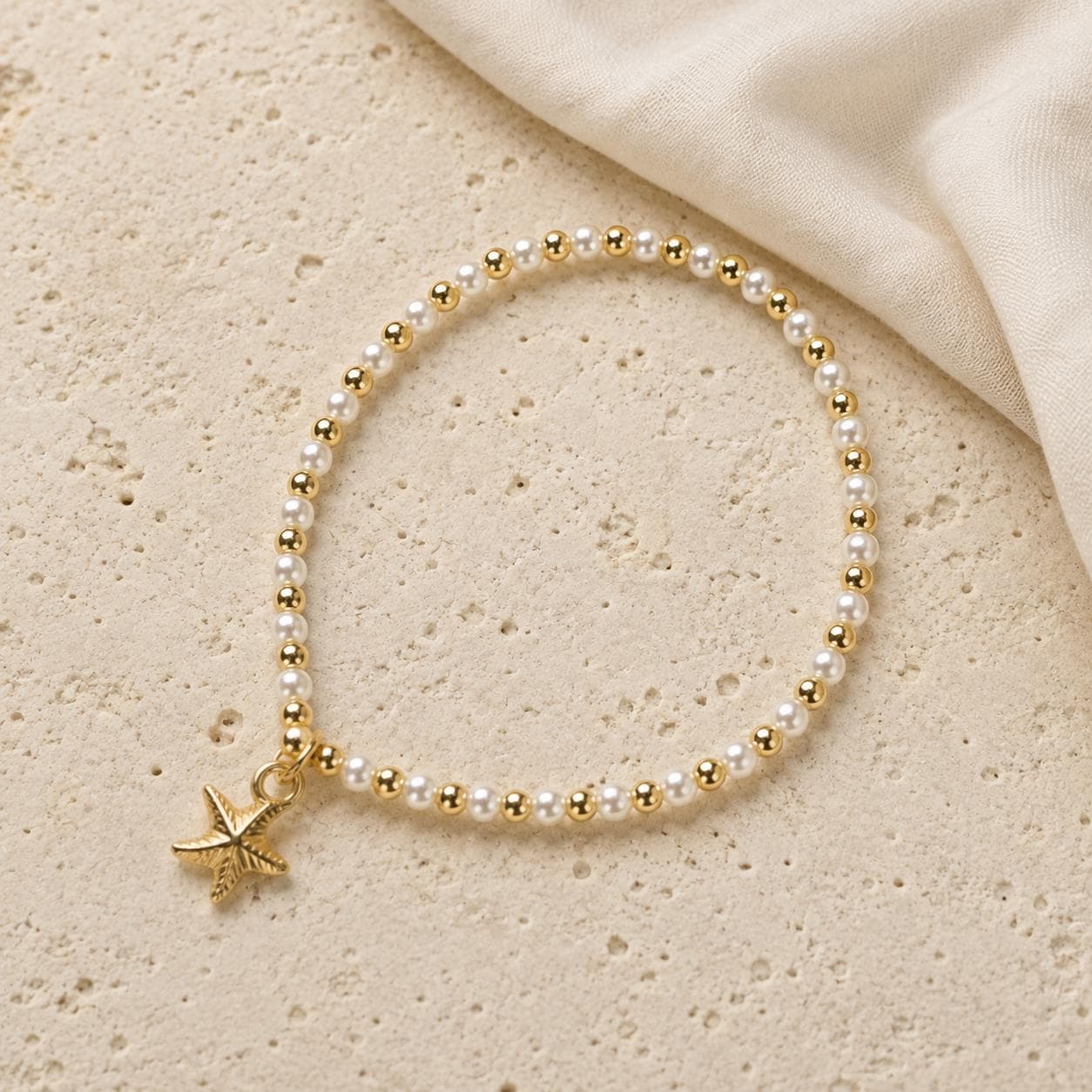 Set of three delicate coastal stretch bracelets featuring small ivory faux pearls and gold-tone seaside details. The coordinating jewellery set includes a blush enamel-style scallop shell charm with pearl centre, a textured gold starfish charm and a ridged gold shell centrepiece with pale champagne faceted beads. Lightweight 16 cm elasticated bohemian costume jewellery for coastal gifts, Christmas presents, stocking fillers, holidays, beach weddings, bridesmaids and gifts for her.