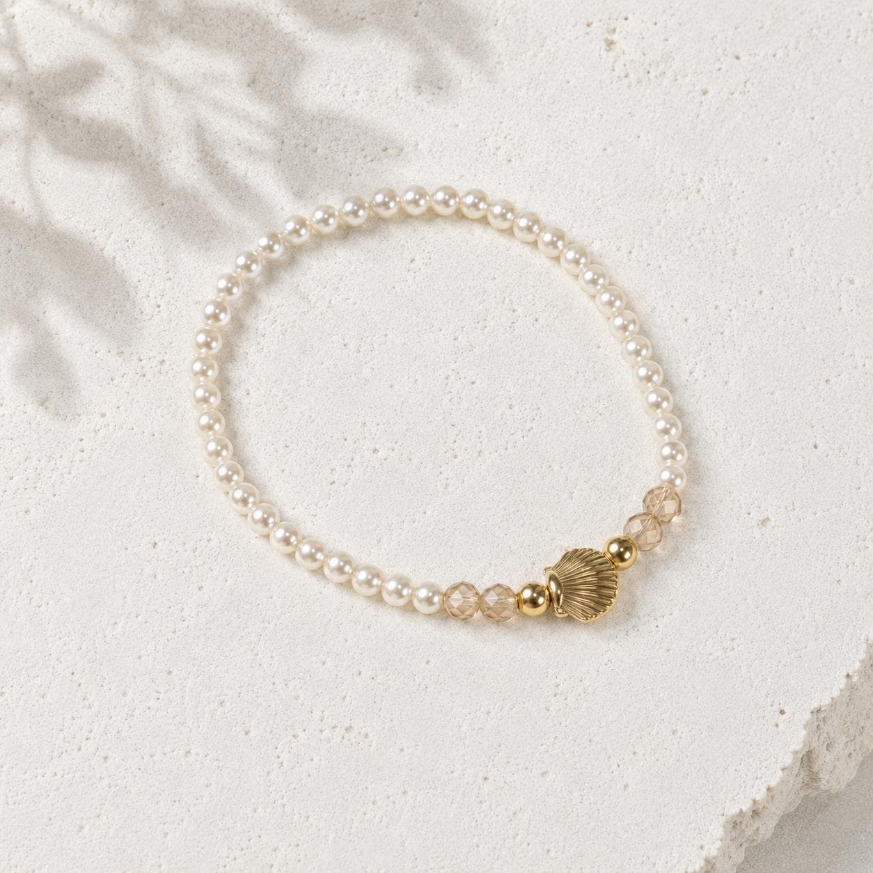 Set of three delicate coastal stretch bracelets featuring small ivory faux pearls and gold-tone seaside details. The coordinating jewellery set includes a blush enamel-style scallop shell charm with pearl centre, a textured gold starfish charm and a ridged gold shell centrepiece with pale champagne faceted beads. Lightweight 16 cm elasticated bohemian costume jewellery for coastal gifts, Christmas presents, stocking fillers, holidays, beach weddings, bridesmaids and gifts for her.
