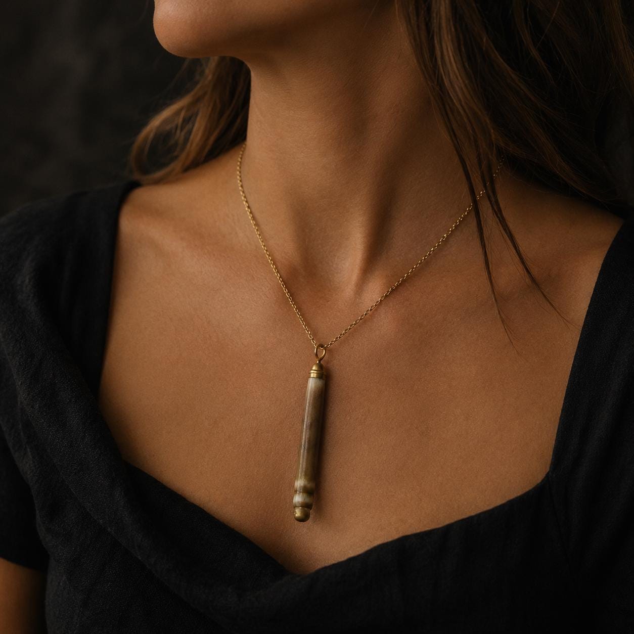 Natural sea-urchin spine pendant worn against black clothing, showing its elongated organic form, banded markings and hand-applied gold-leaf finish.