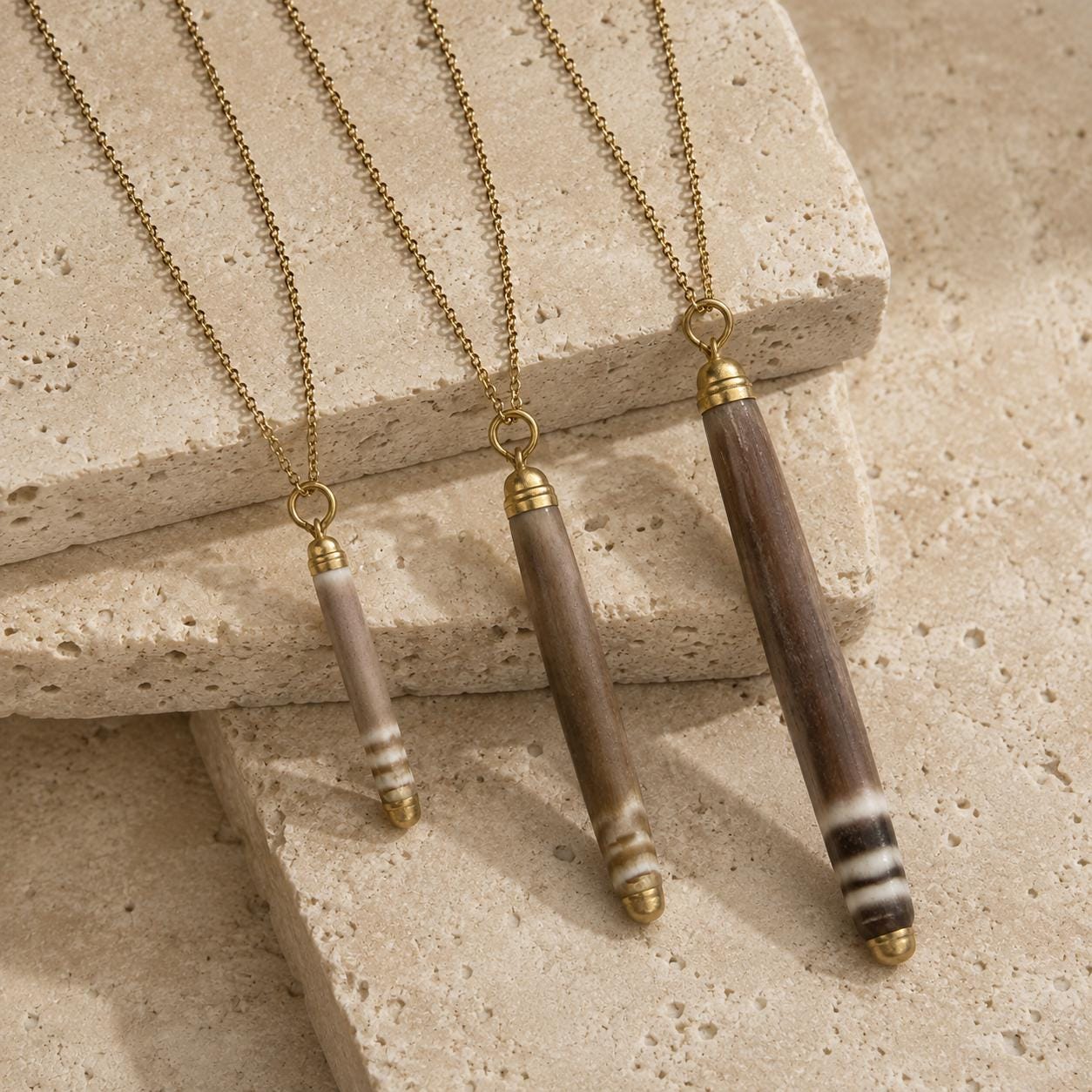 Three handmade sea-urchin spine necklaces in Small, Medium and Large, displayed on warm beige stone with liquid-gold tips and 18K gold-plated chains.