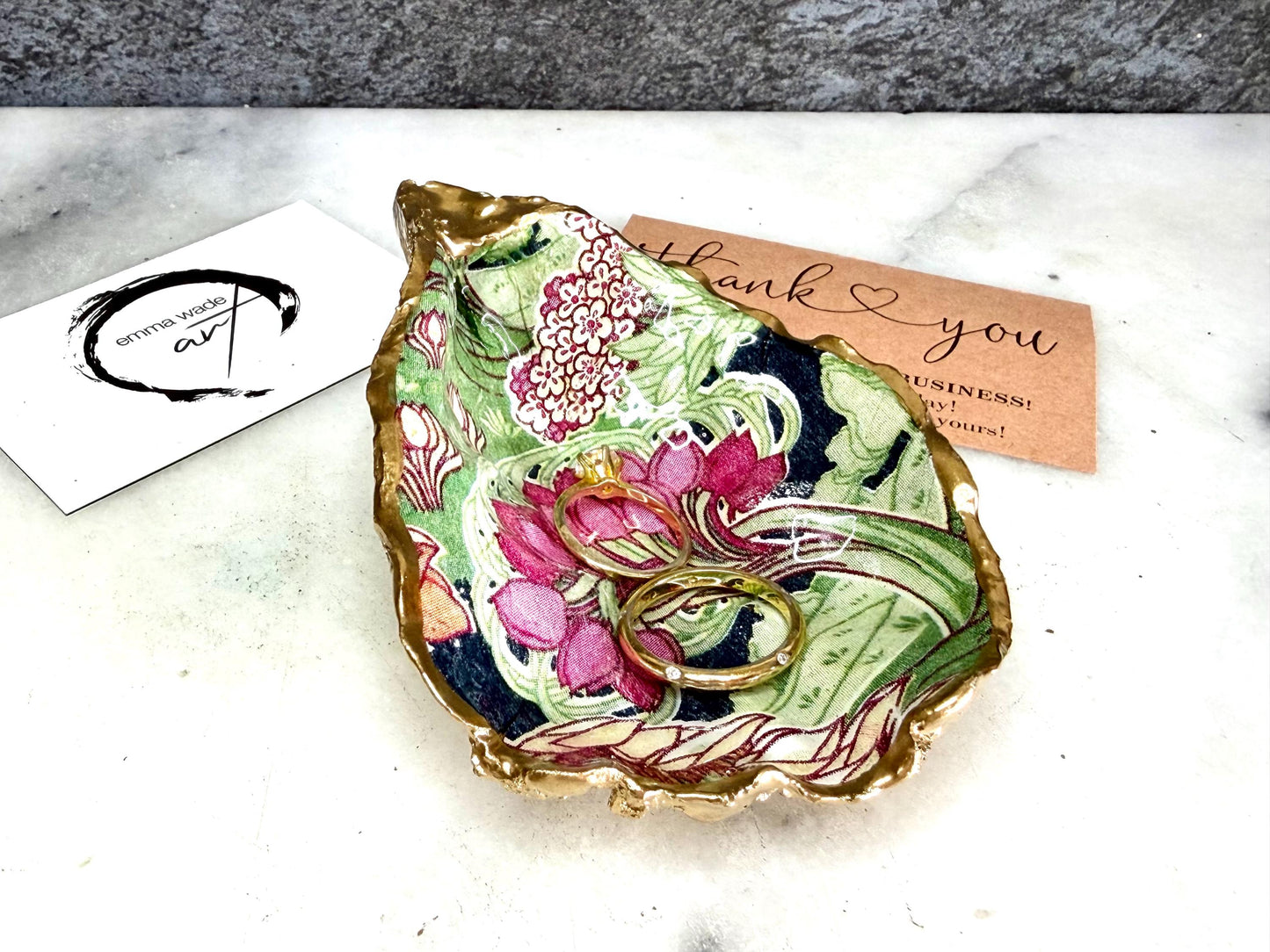 Handcrafted V&A Museum Swirling Trees shell dish collection featuring large and small scallop shells and oyster shells decorated with flowing botanical artwork, pink water lilies and rich green foliage. Each natural Dorset shell is hand-gilded with real liquid gold leaf and sealed with crystal-clear resin. Luxury coastal decor, jewellery dishes, ring holders and trinket trays. Available individually or as a coordinated set of four shells.