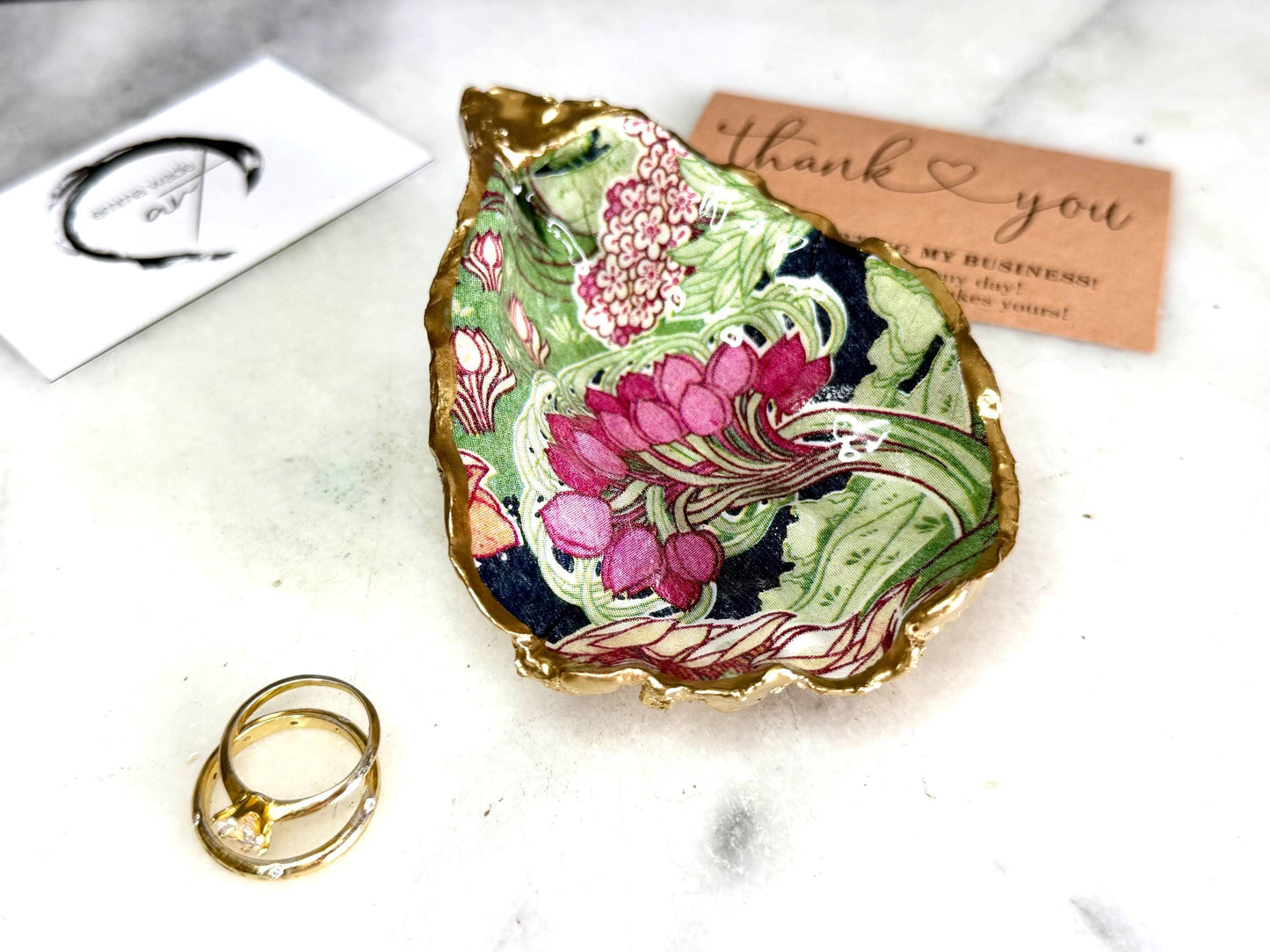Handcrafted V&A Museum Swirling Trees shell dish collection featuring large and small scallop shells and oyster shells decorated with flowing botanical artwork, pink water lilies and rich green foliage. Each natural Dorset shell is hand-gilded with real liquid gold leaf and sealed with crystal-clear resin. Luxury coastal decor, jewellery dishes, ring holders and trinket trays. Available individually or as a coordinated set of four shells.